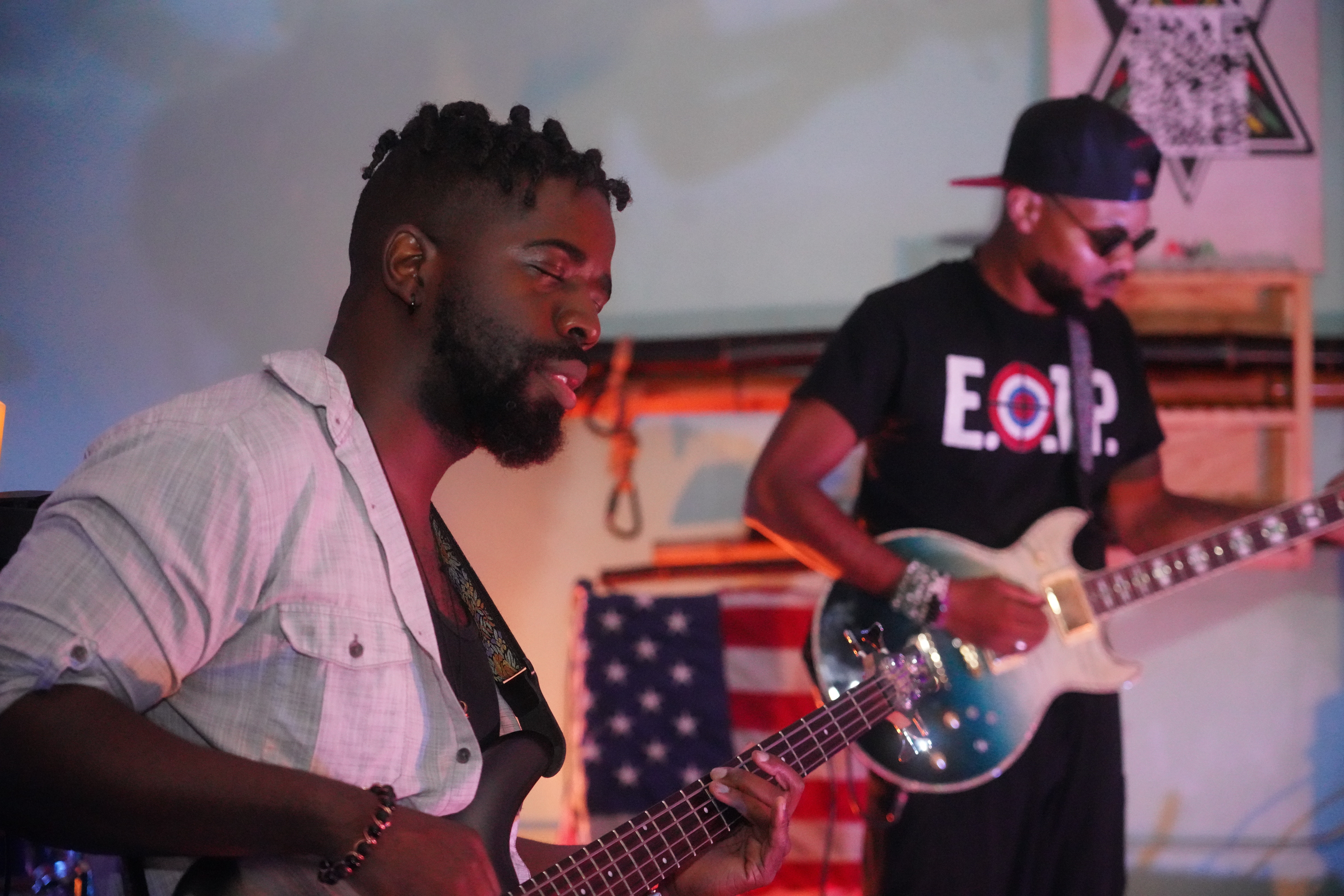 Two men playing electric guitars in a room with a projection screen and decorations in the background.