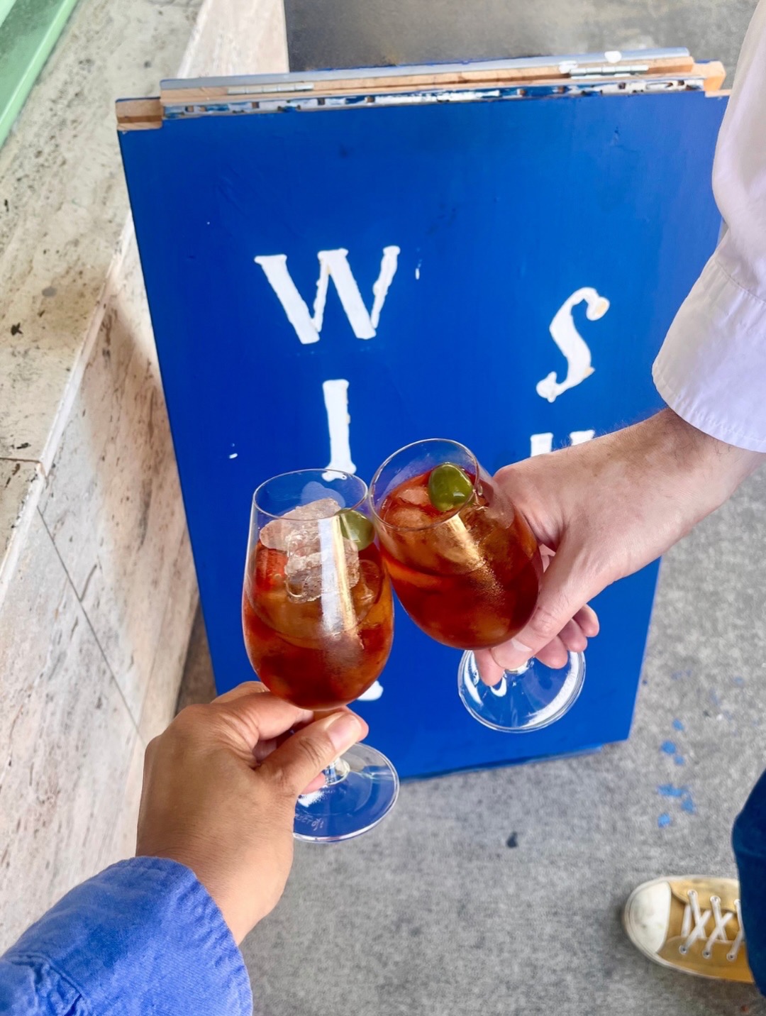 Two people holding glasses of iced tea with lime slices, standing outside near a blue sign with white text.