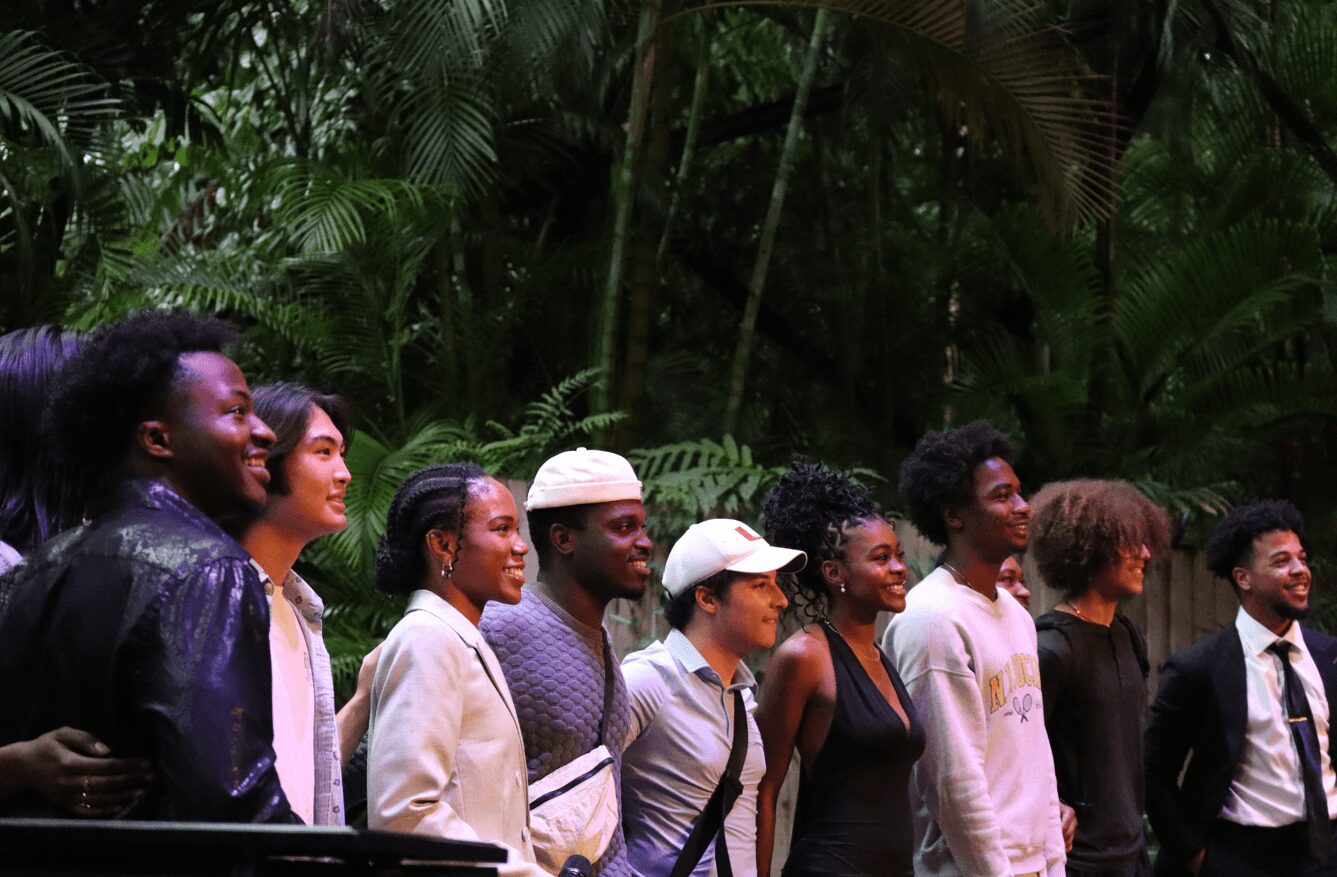 Group of people standing outdoors among lush green trees, smiling and looking to the right.