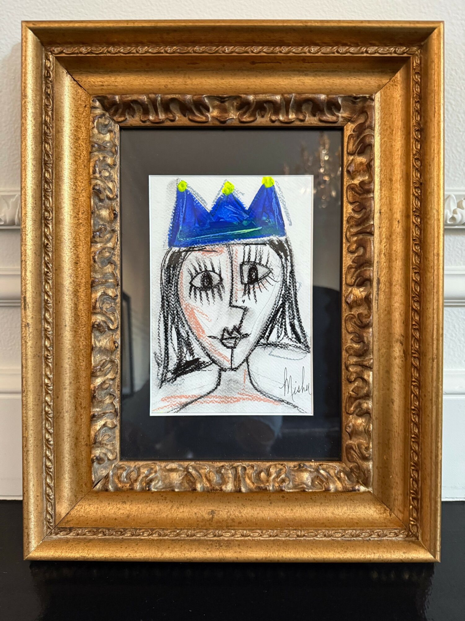 Framed drawing of a girl with a crown, long hair, and closed eyes, in a black frame with a gold ornate border.