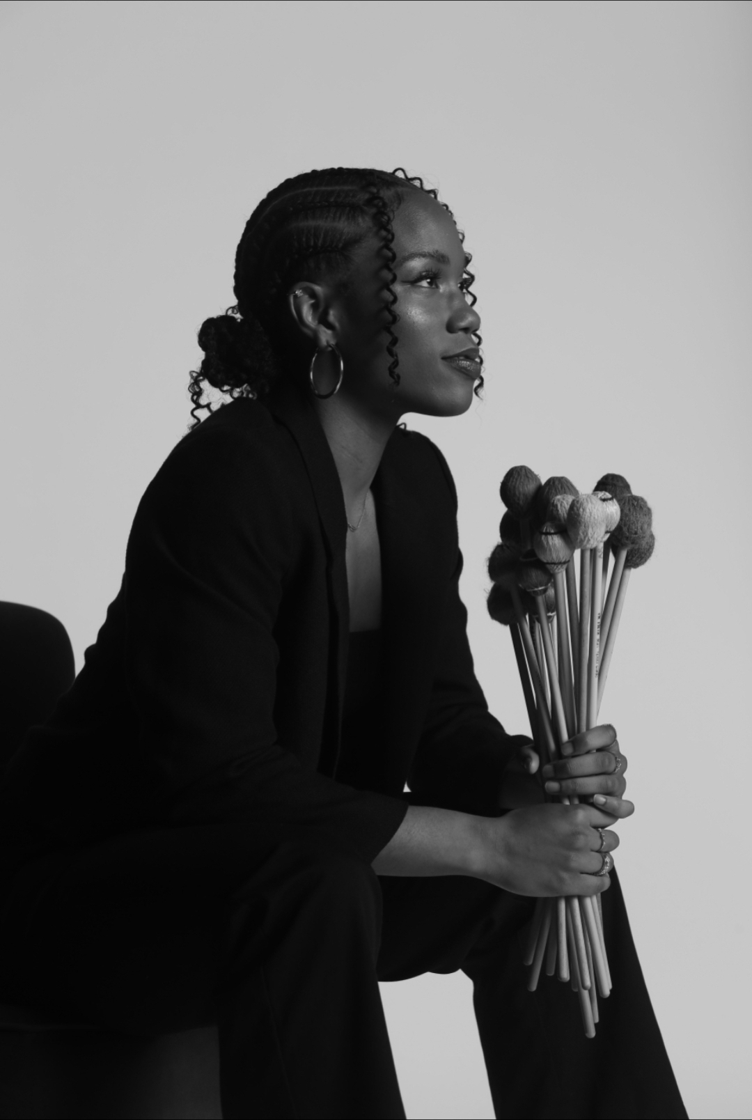 Woman with braided hair holding a bouquet of flowers, sitting in profile against a plain background.