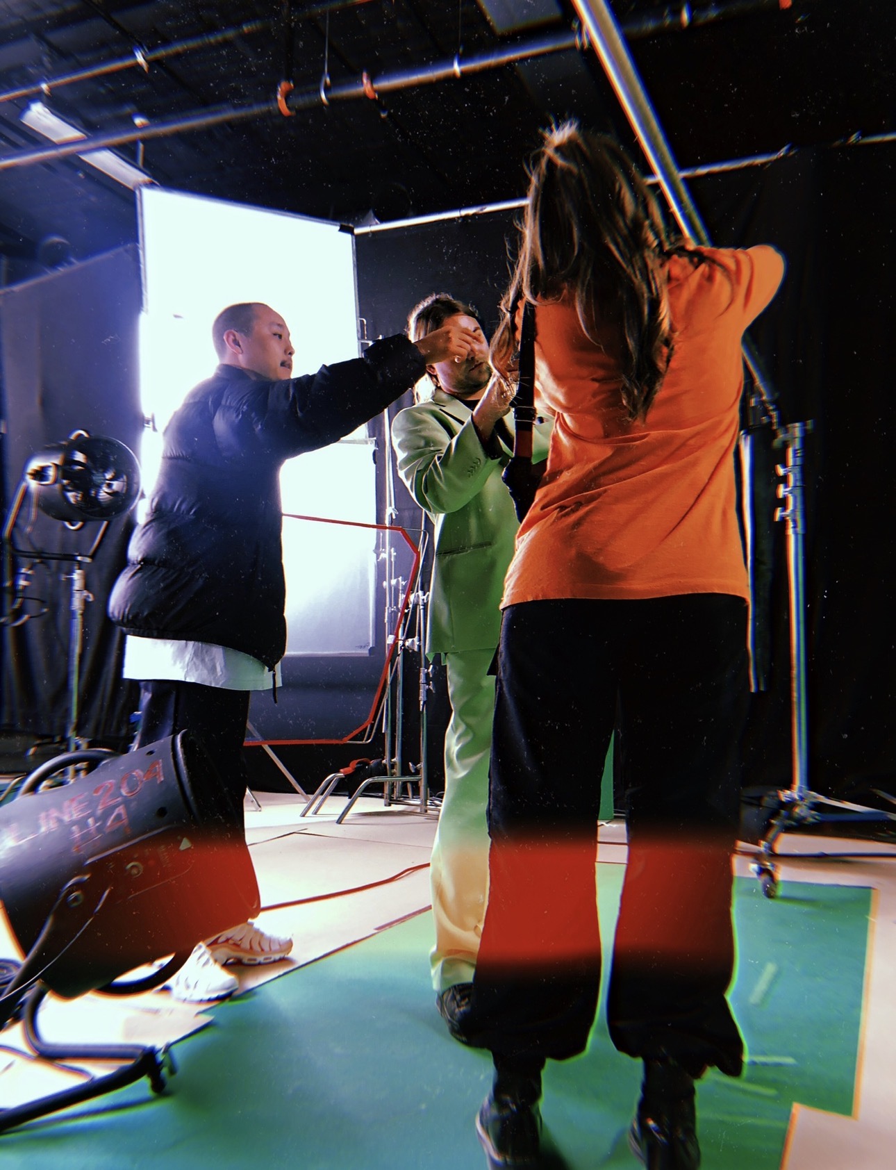 Three people on a film set, one holding a boom microphone, another adjusting equipment, and a third standing nearby.