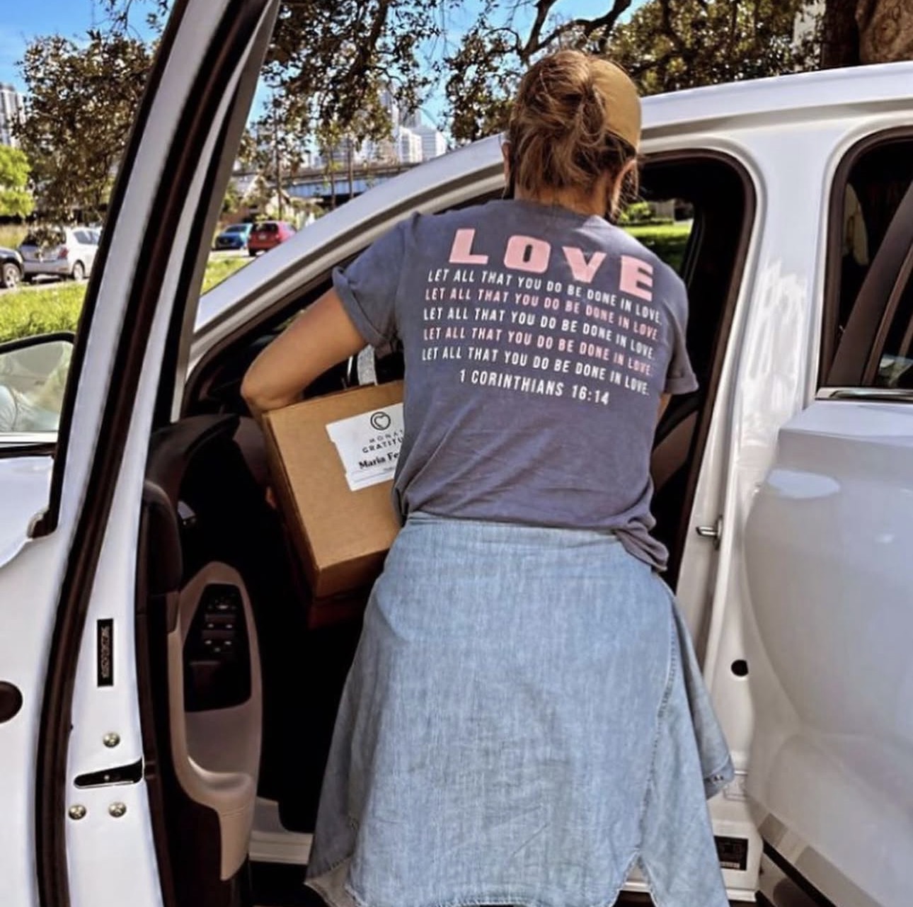 Person loading a box into a vehicle, wearing a T-shirt with the word 'LOVE' and a denim skirt.