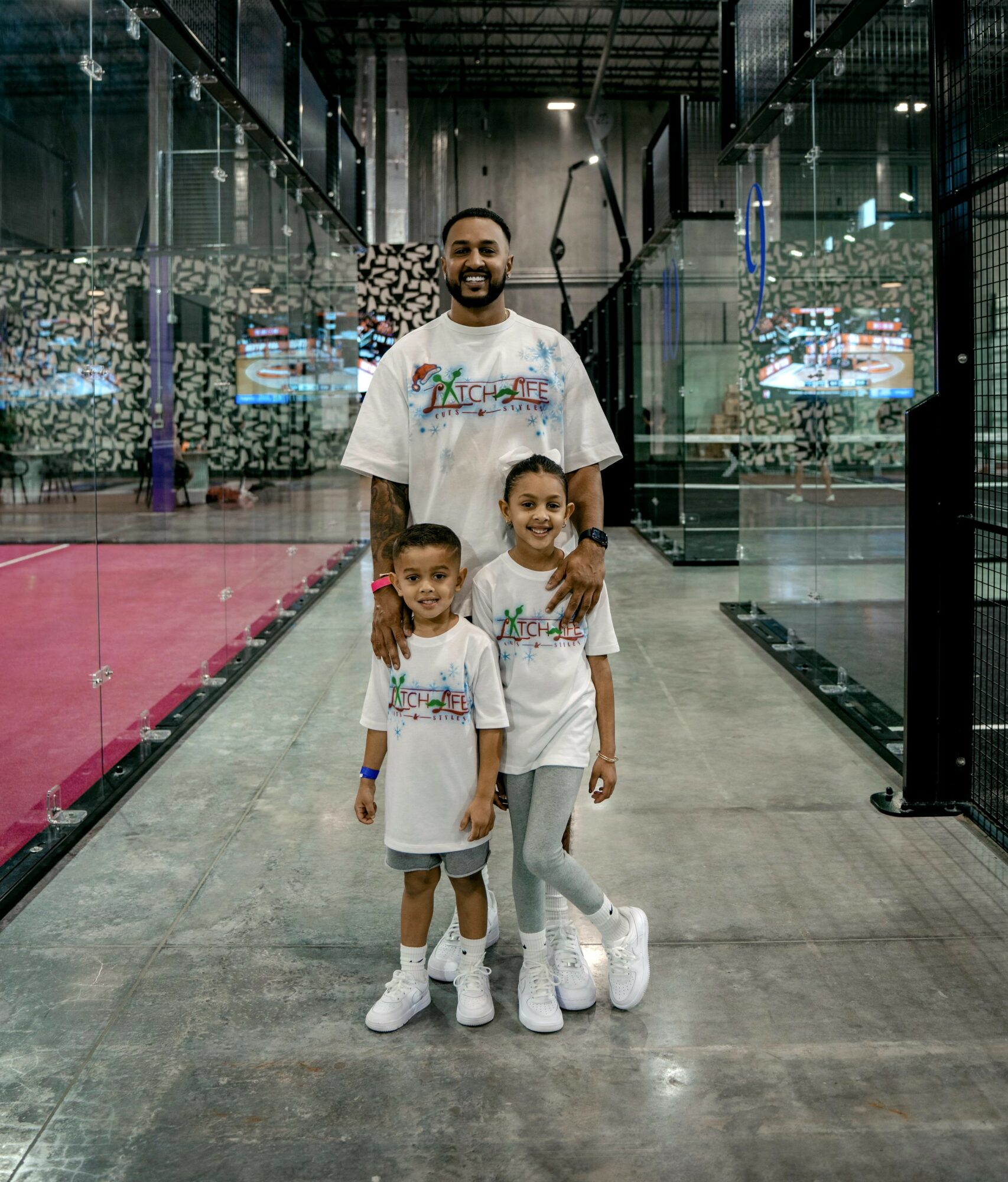 Man with two children in matching outfits inside a modern building with glass walls and colorful decor.