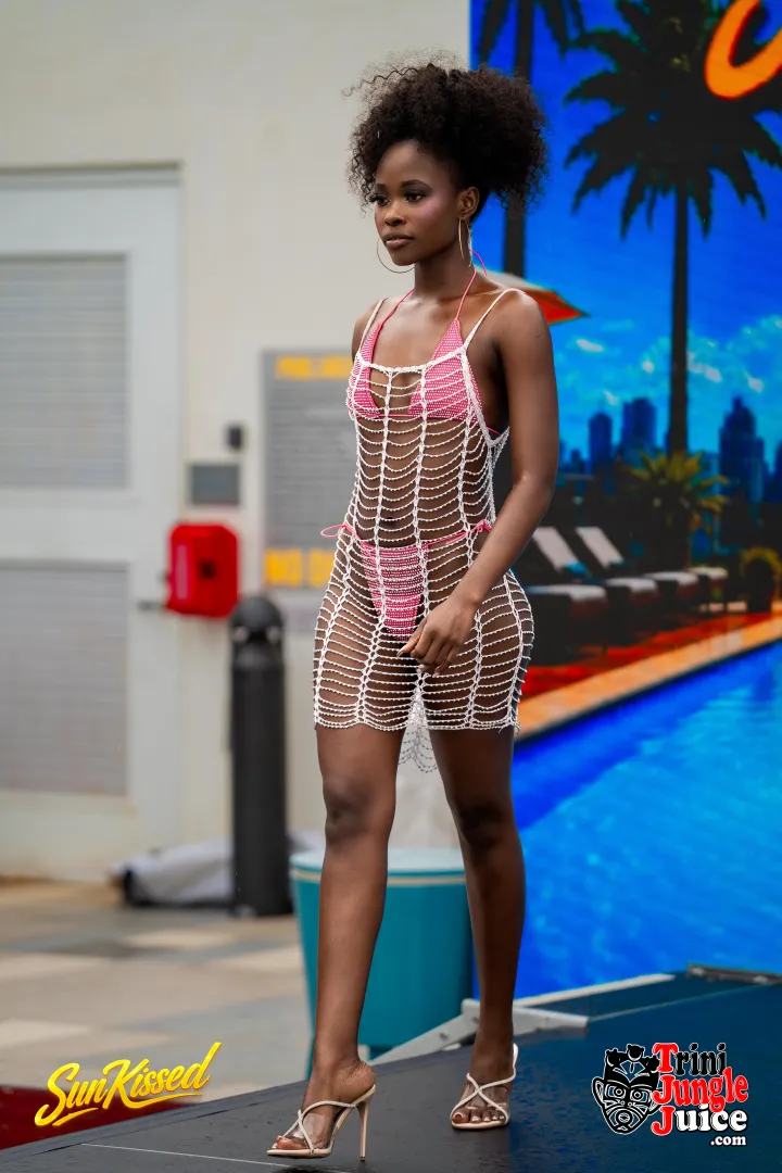 Young woman in a pink bikini and a see-through cover-up stands outdoors near a pool, with a colorful mural in the background.