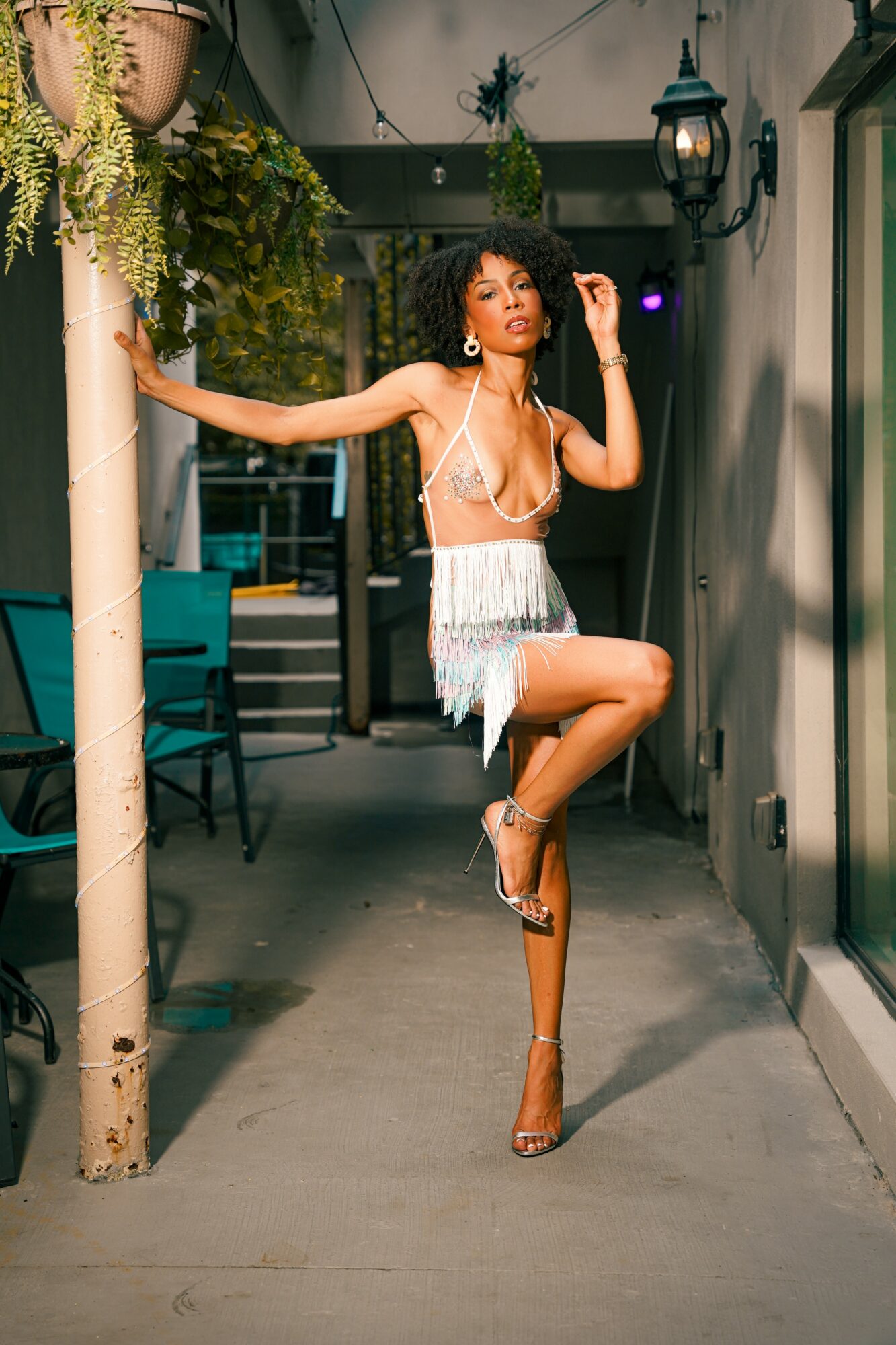 Woman in a fringed dress poses with one leg raised and arm extended in an outdoor setting at night.