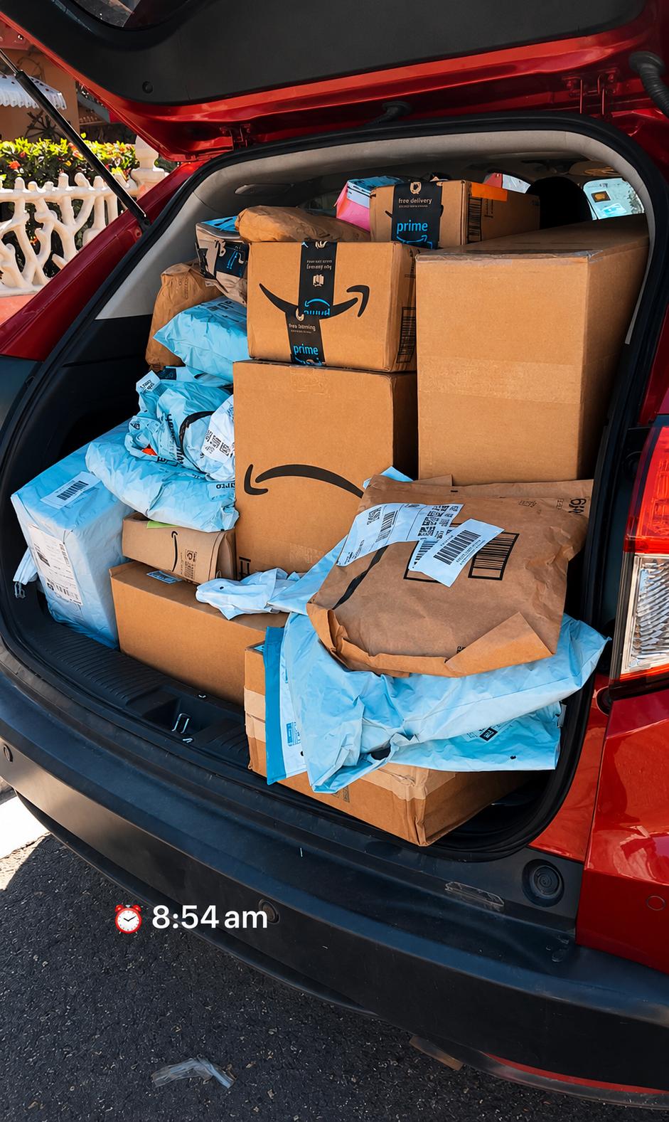 Car trunk filled with boxes and packages, some wrapped in blue tissue paper, in a red vehicle.