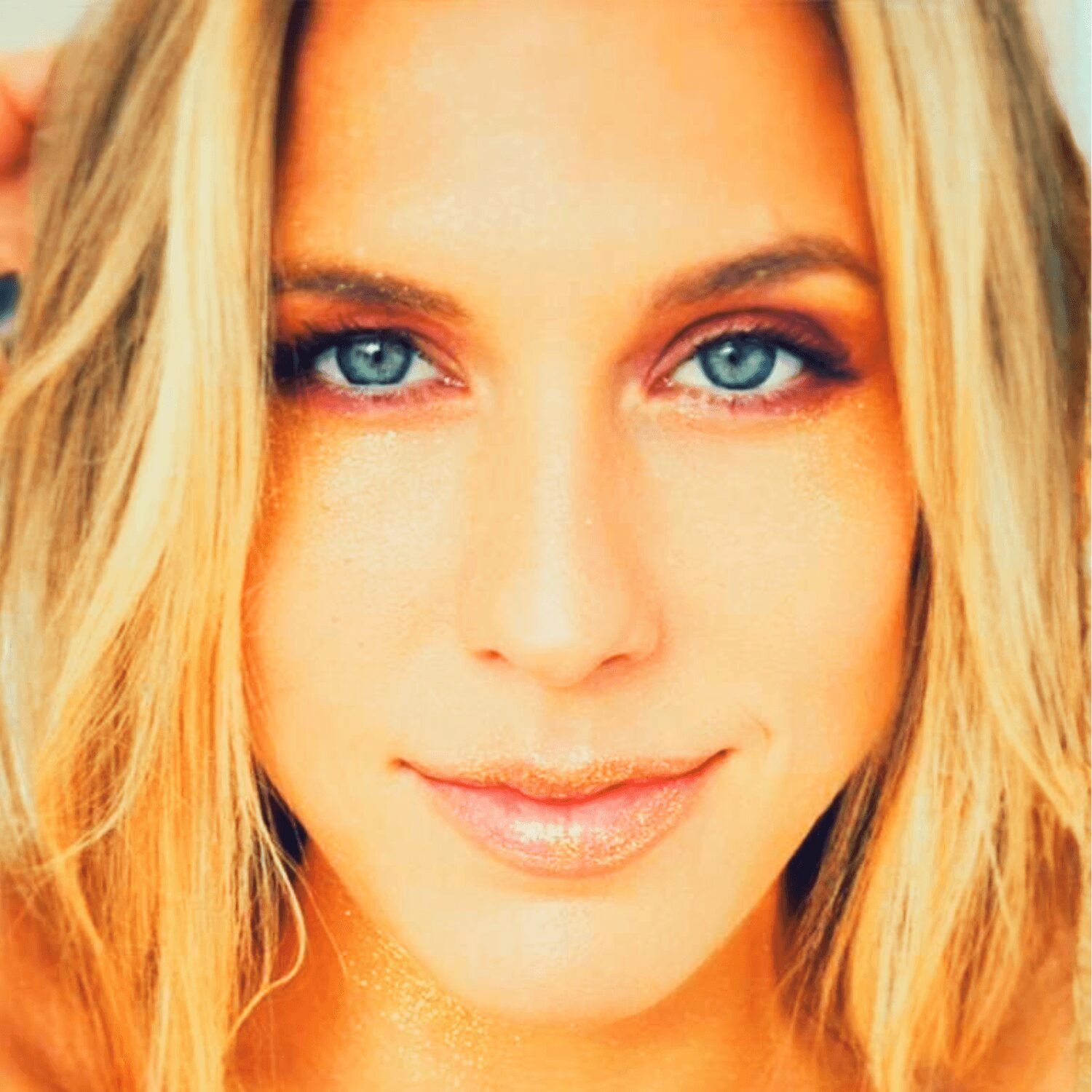 Close-up of a woman with blue eyes and blonde hair, smiling softly, looking directly at the camera.