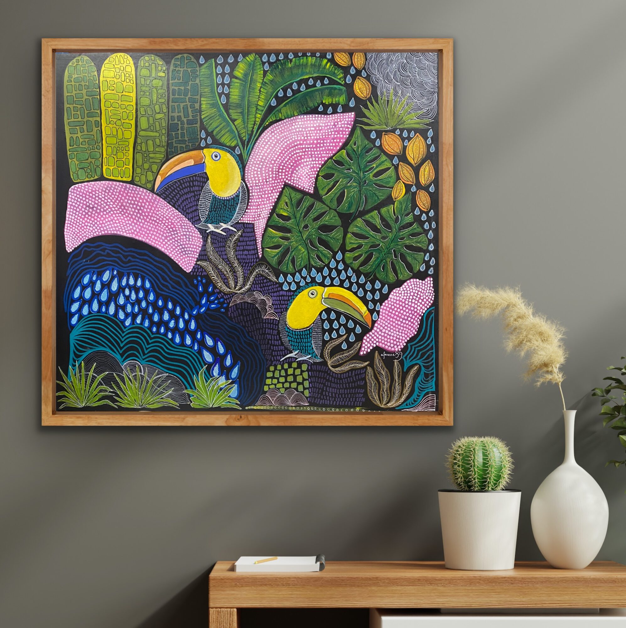 Colorful painting of toucans, tropical plants, and flowers on a gray wall, with a wooden table and potted cactus nearby.