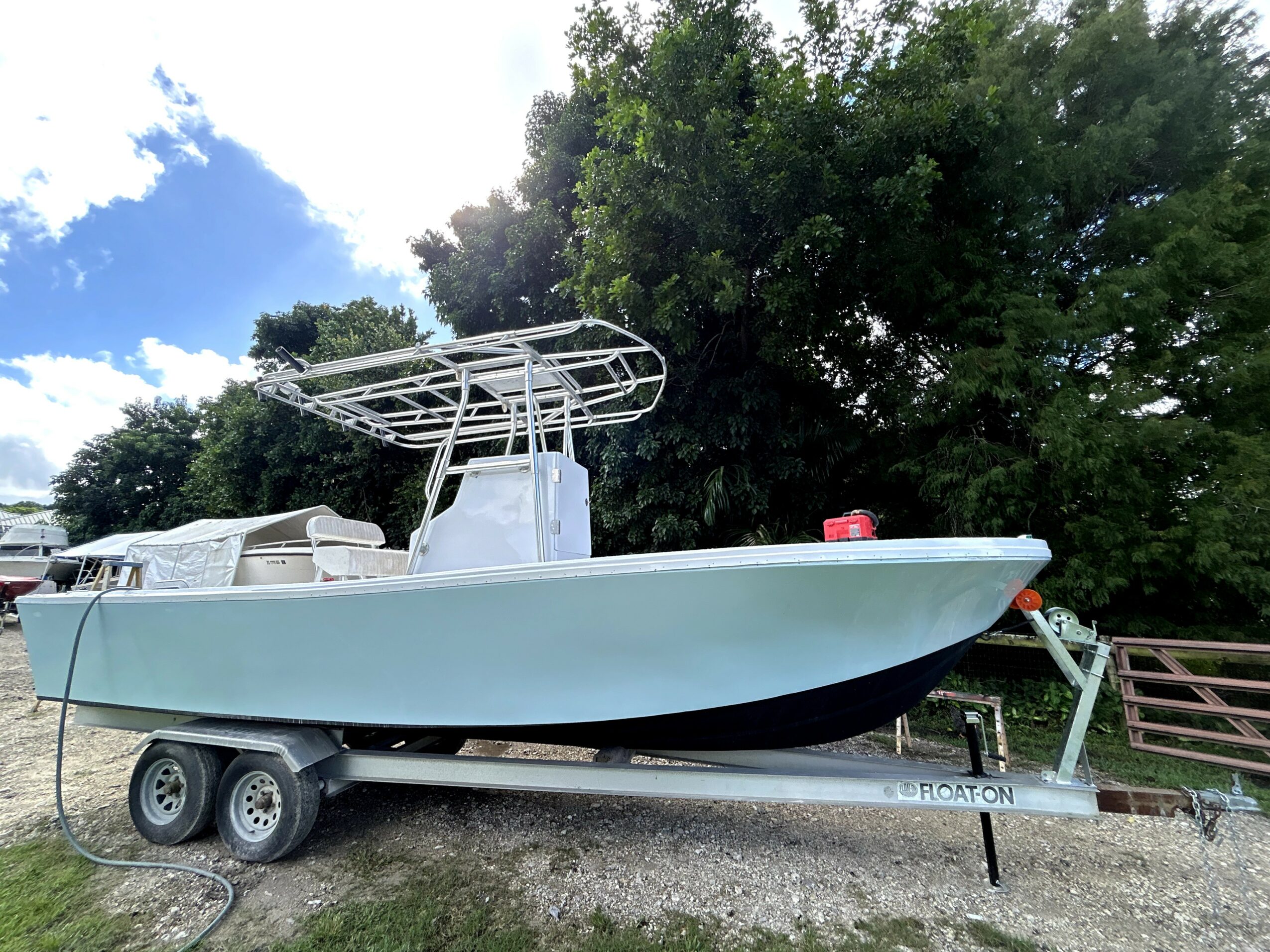 A white boat on a trailer outdoors with trees and a partly cloudy sky in the background.