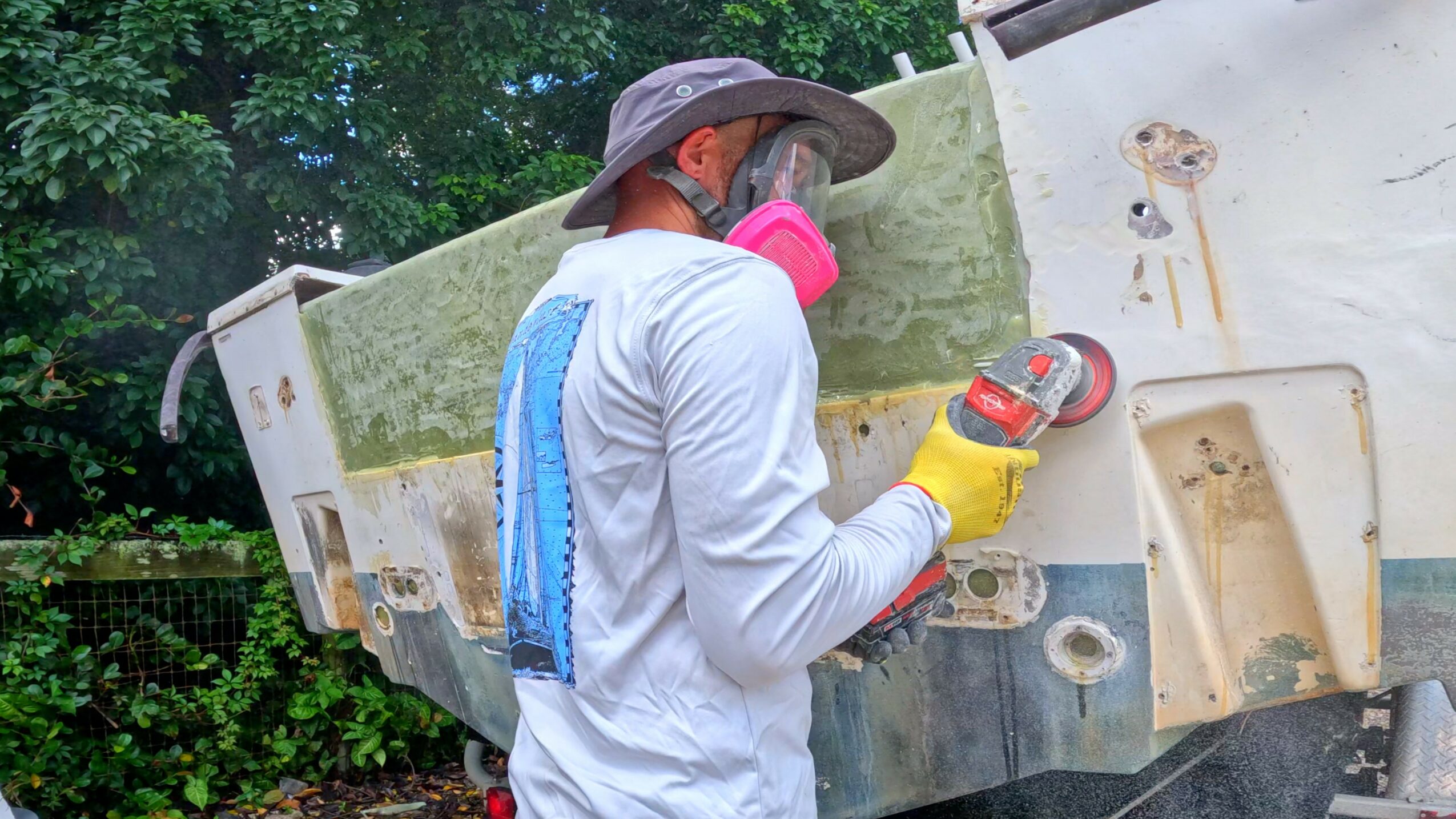 Person wearing a hat, gloves, and a mask, working on a large vehicle outdoors, holding a tool.