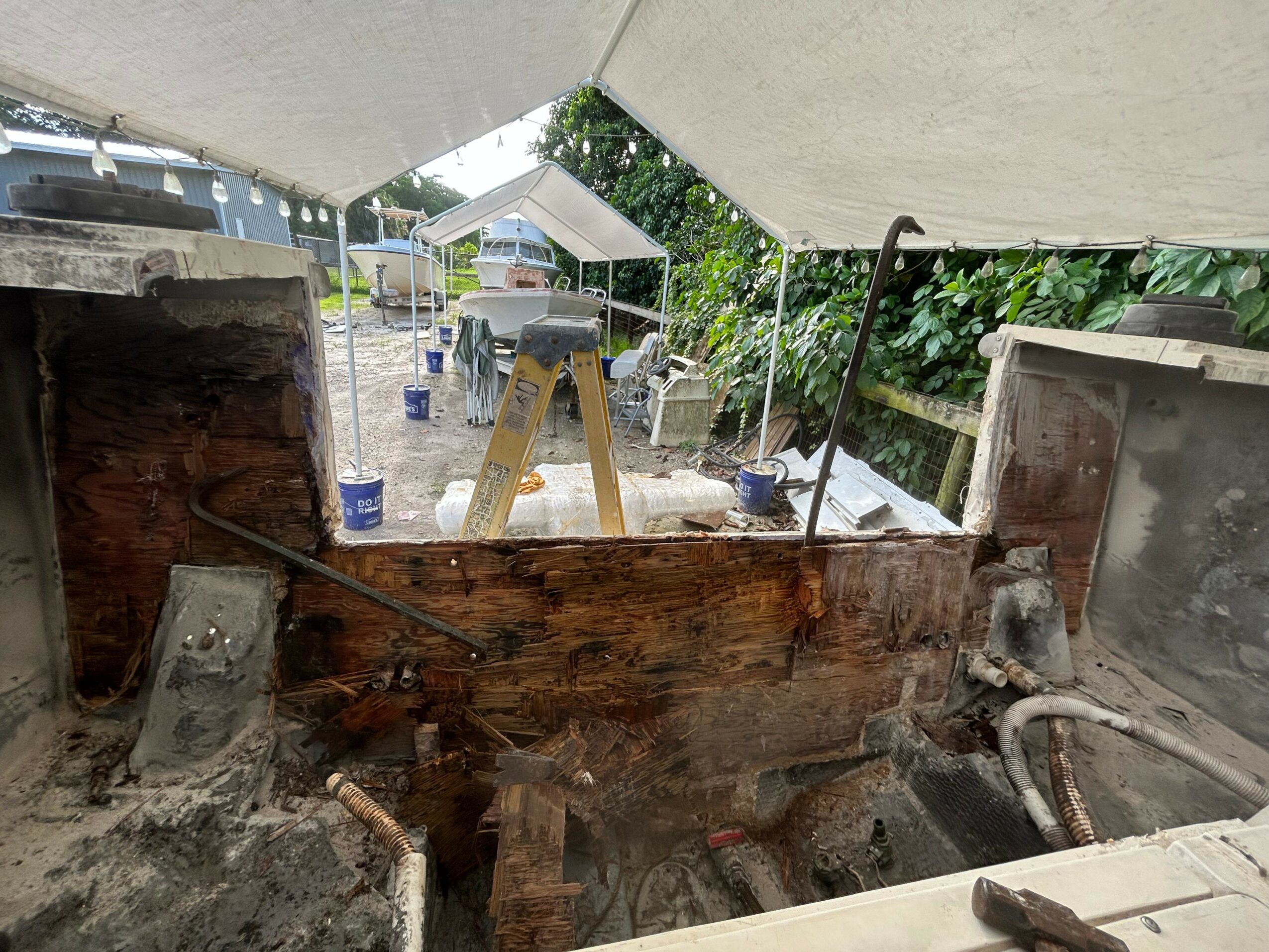 View of a partially dismantled outdoor structure with tools and debris, seen from underneath a canopy or tent.