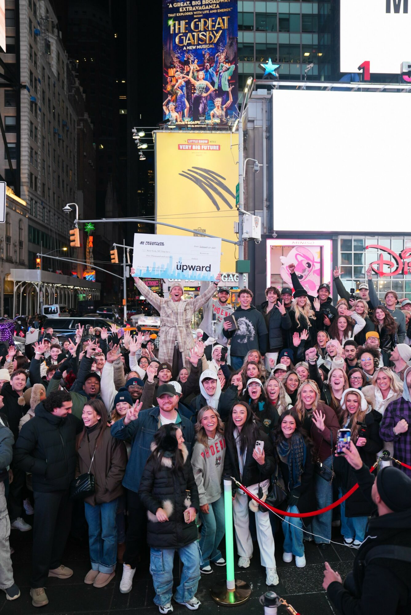 Crowd of people gathered in Times Square at night, some holding signs, with bright billboards and buildings in the background.