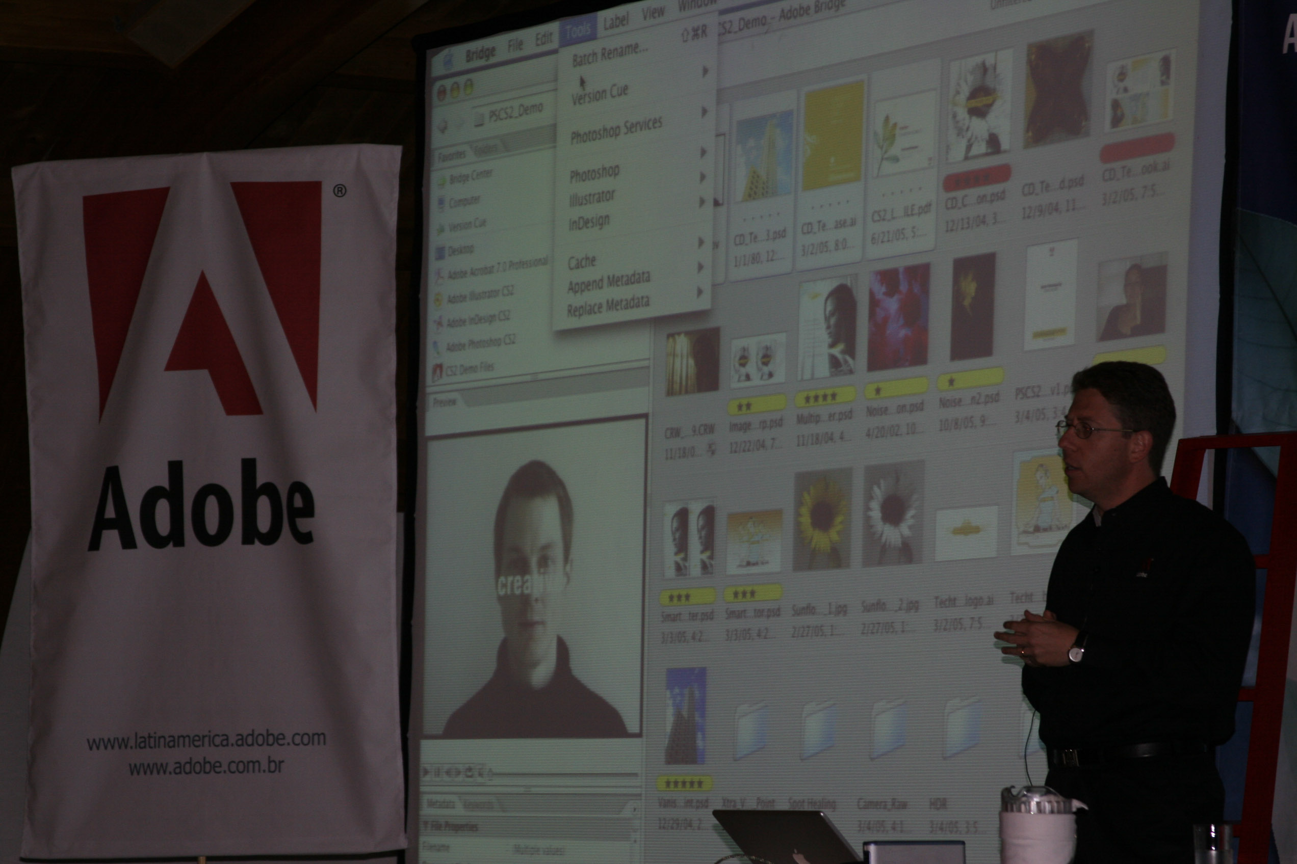 Person standing in front of a large screen displaying a computer interface, with an Adobe banner nearby.