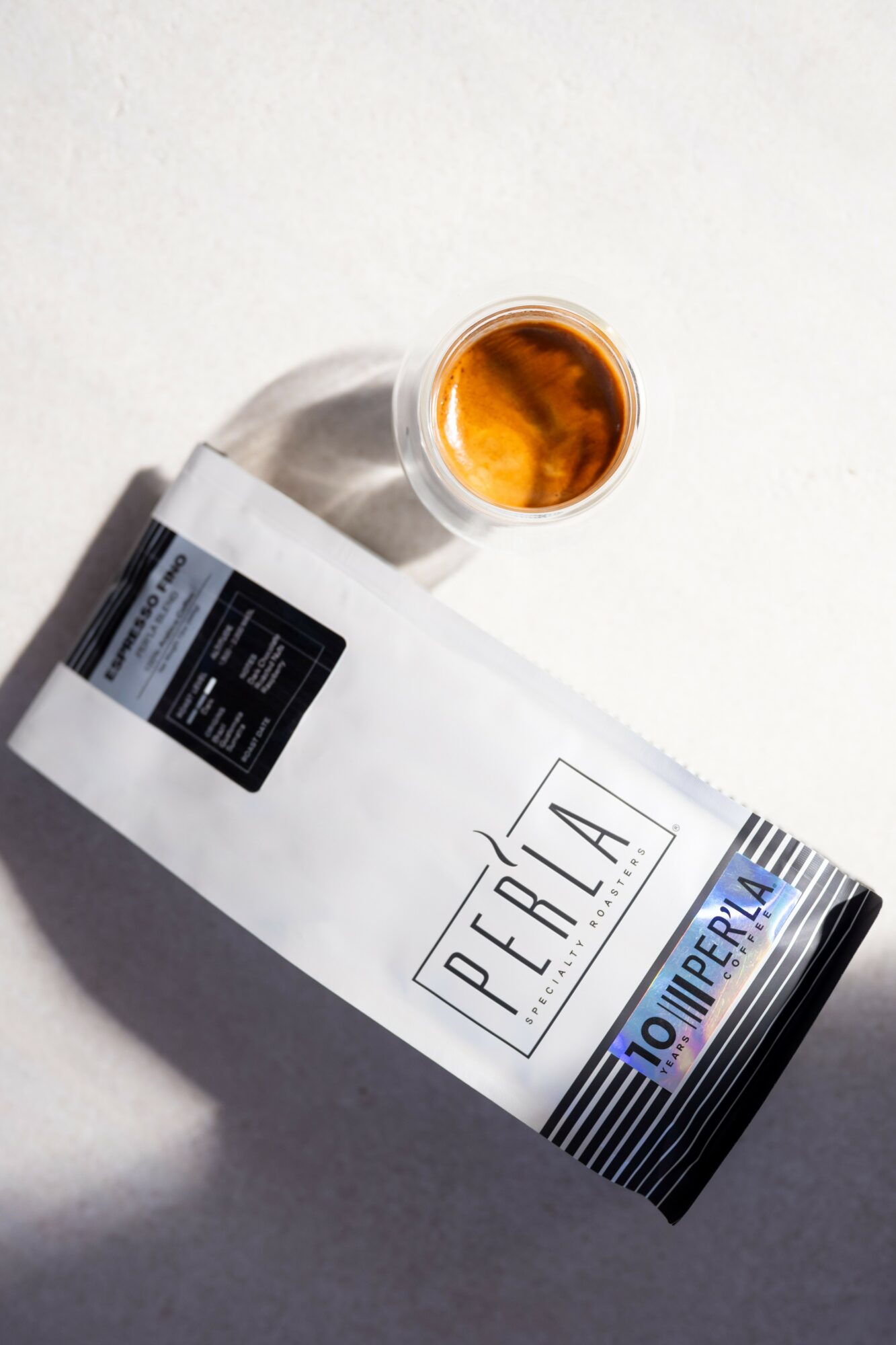 A bottle labeled 'Perla' with a glass of amber liquid on top, placed on a white surface.