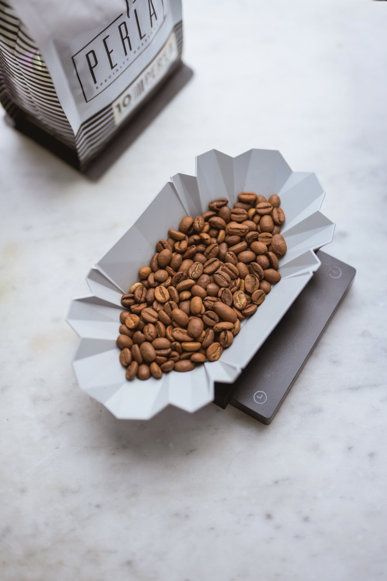 Coffee beans in a paper tray on a digital scale, with a bag of coffee in the background.
