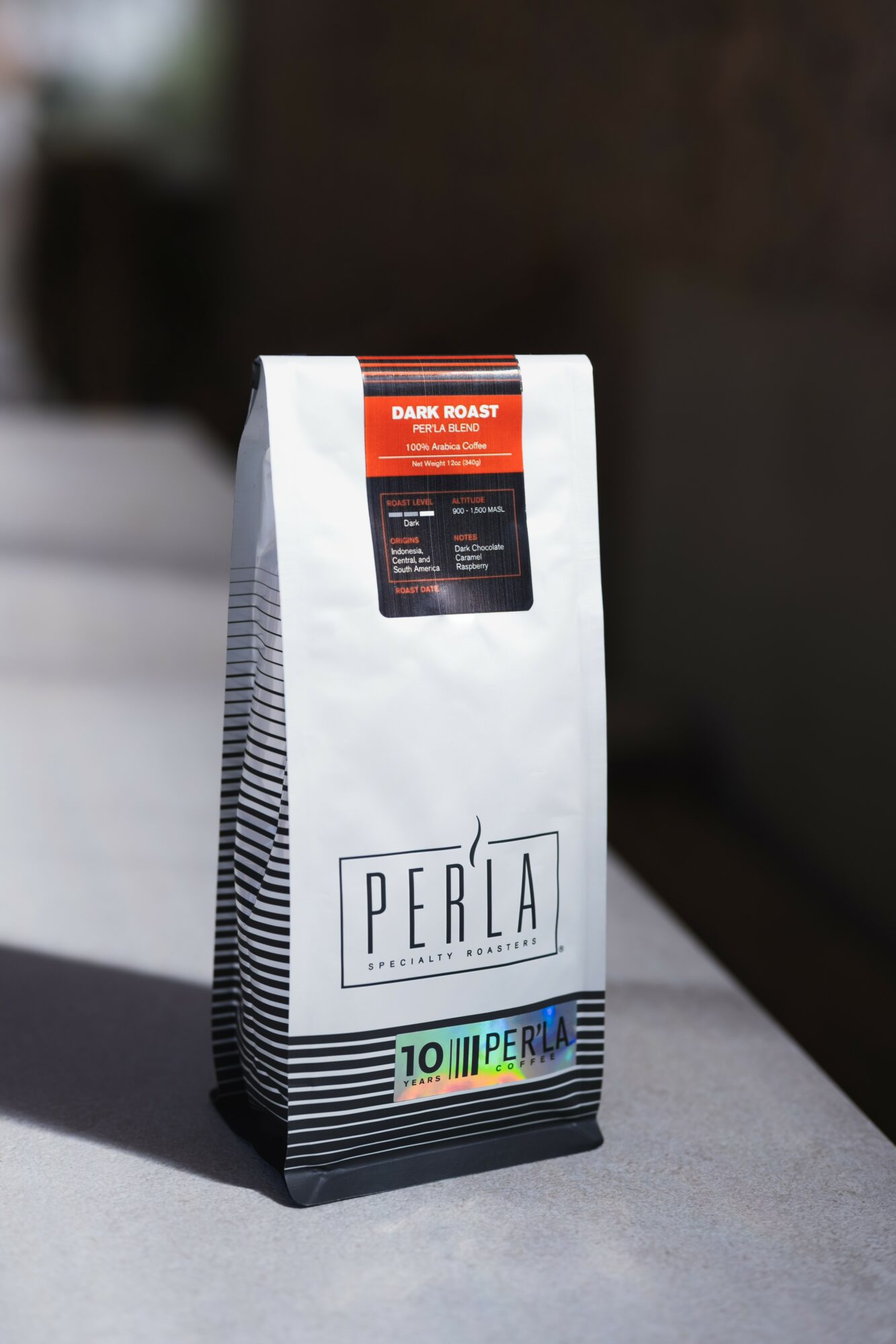 White coffee bag with black and blue text, labeled 'PERLA' and '10 M PERLA', standing on a gray surface.