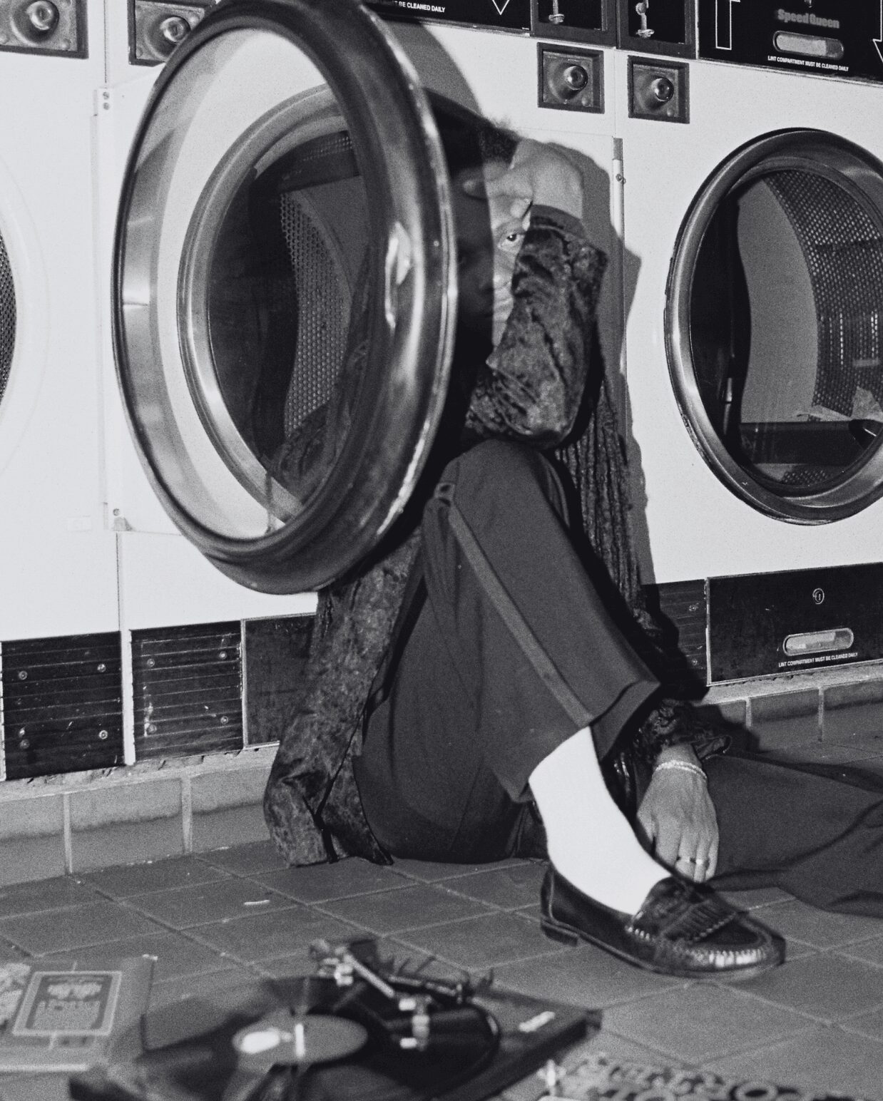 Person sitting on the floor with head and arm inside a washing machine, surrounded by laundry machines, in black and white.