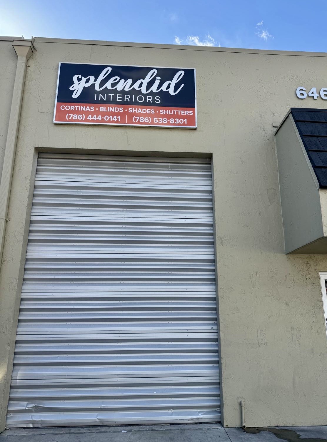 Sign for 'Splendid Interiors' above a closed metal roll-up door, with a blue sky in the background.