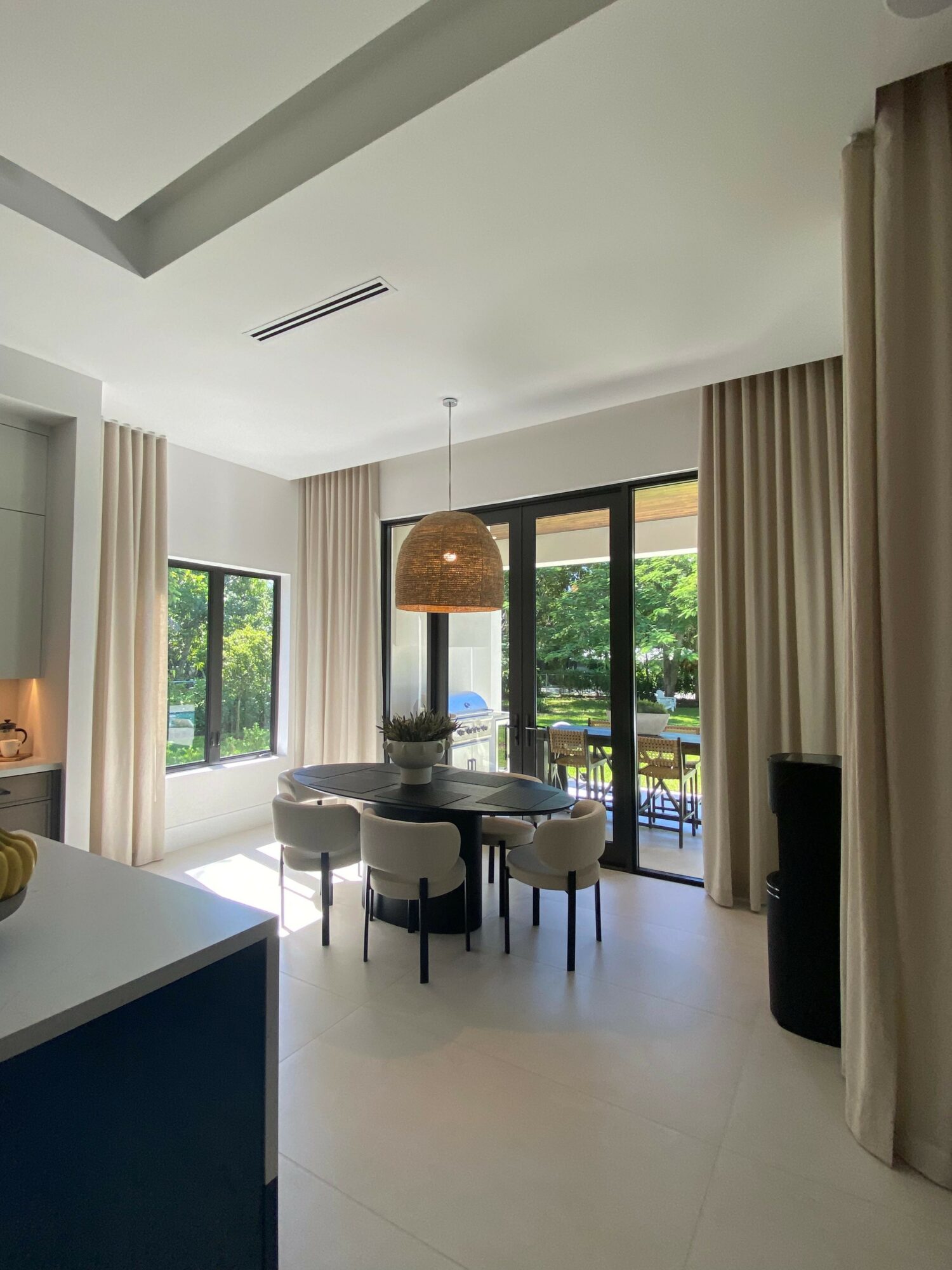 Living room with large windows, a round dining table, six chairs, and a balcony with greenery outside.