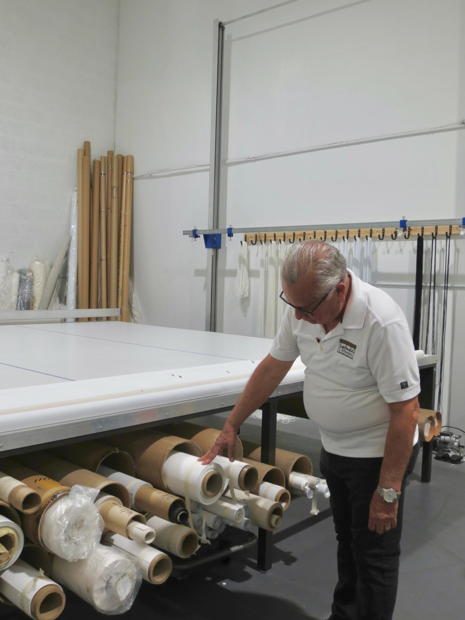 Man inspecting large rolled materials in a workshop with tools and equipment in the background.