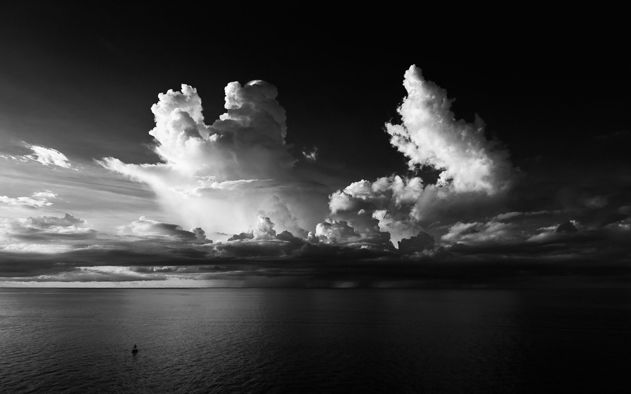 Clouds over a calm body of water with a small boat, in black and white.