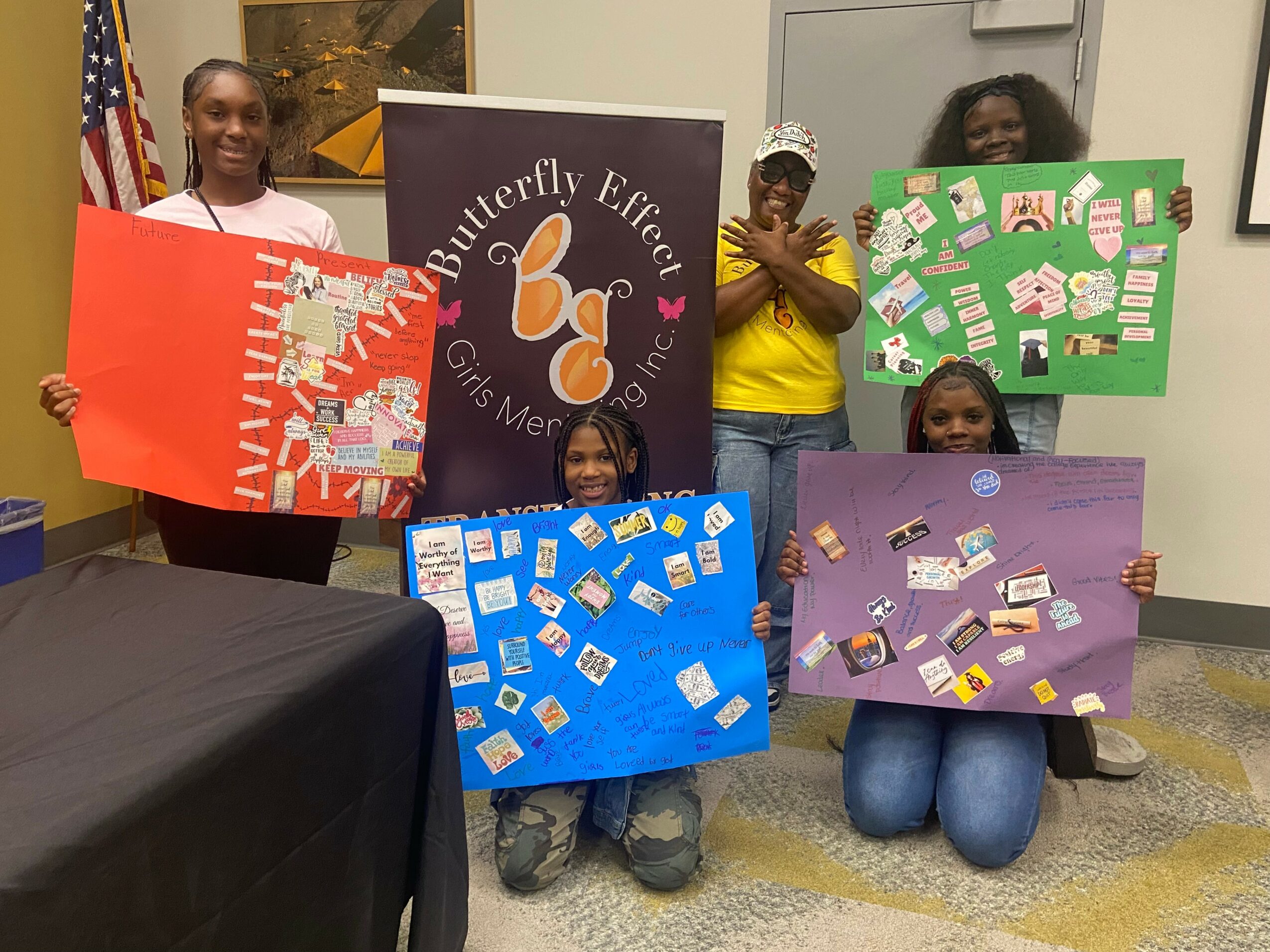 Four children holding colorful posters in a room with a banner reading 'Butterfly Effect Girls Inc.'