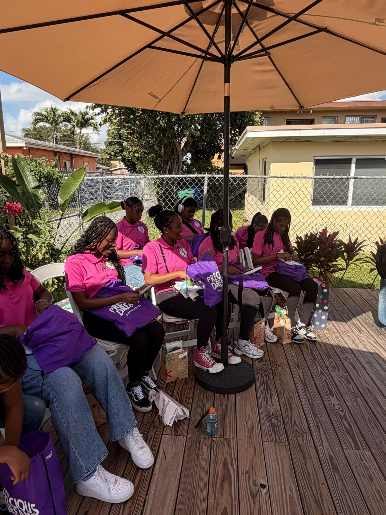 Group of children sitting and standing on a wooden deck outdoors, some with umbrellas, in a garden area.