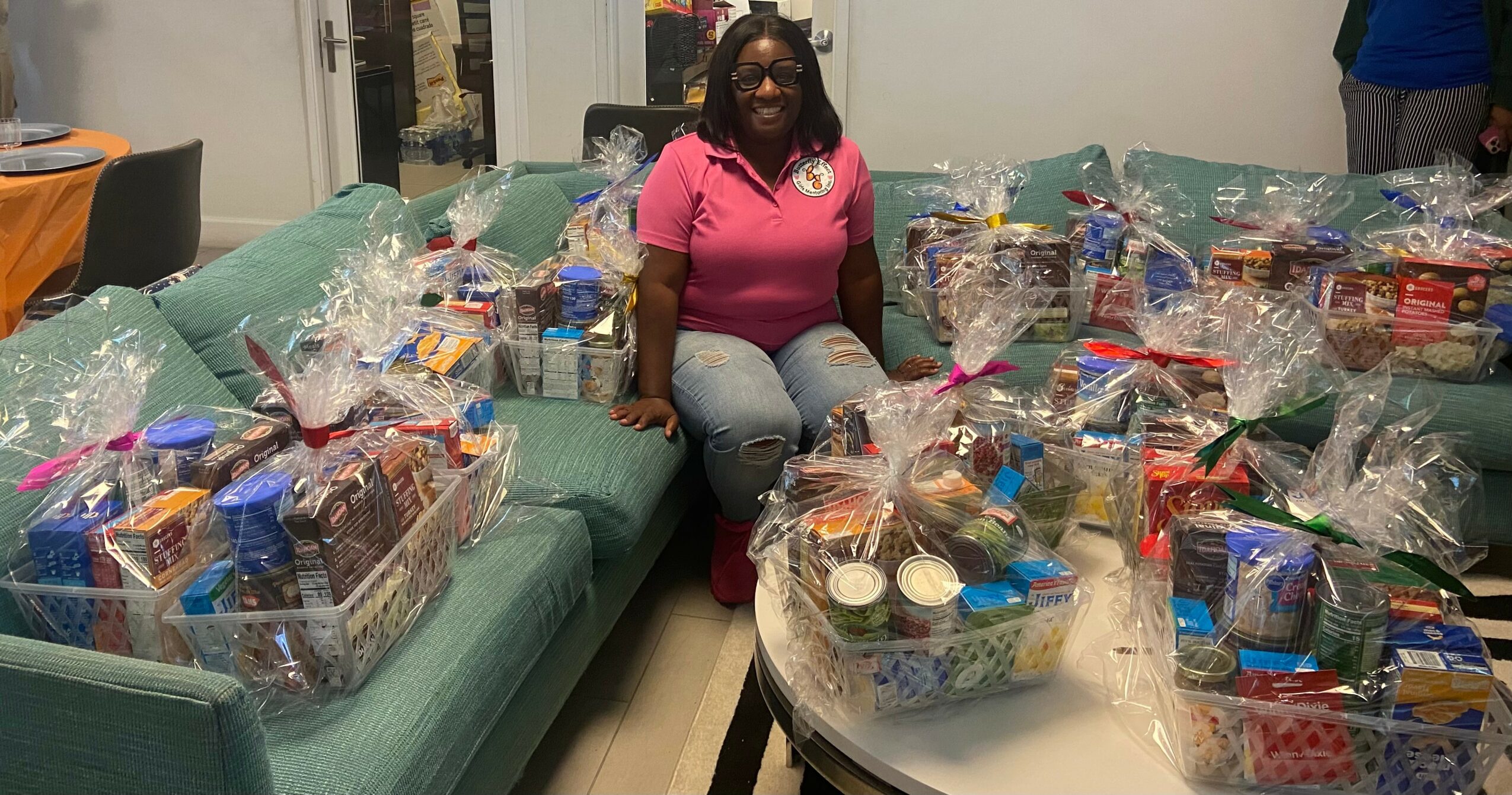 Woman sitting at a table surrounded by gift baskets wrapped in clear plastic, filled with snacks and treats.