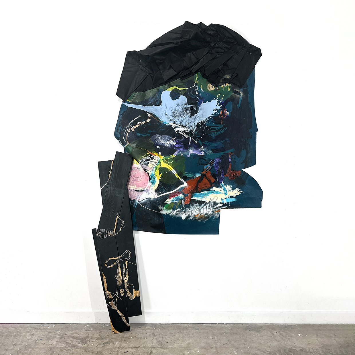 Clothes and a bag with colorful abstract designs hanging on a white wall, with a gray floor below.