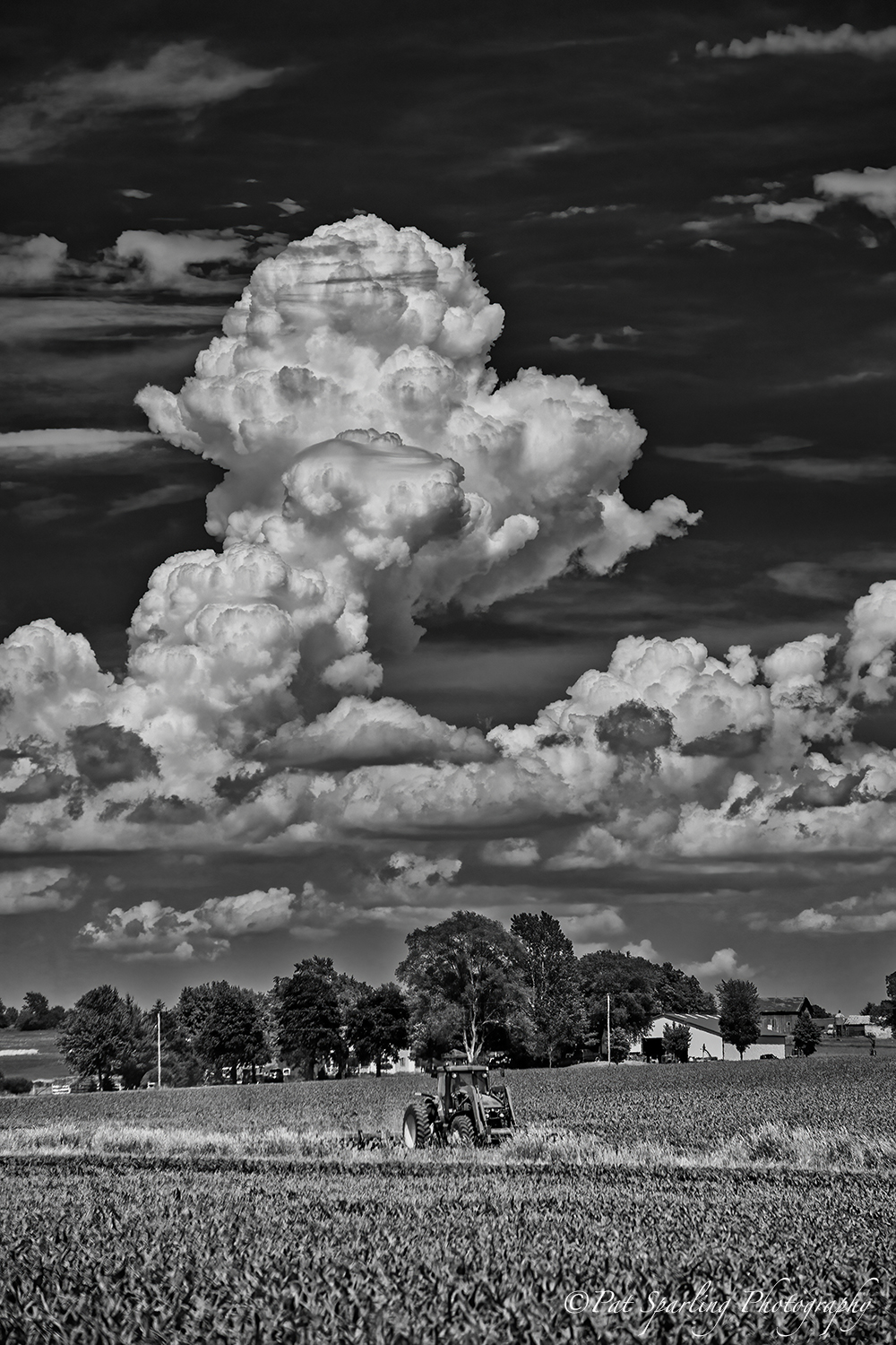 Clouds in the sky over a rural landscape with trees and a field, black and white image.