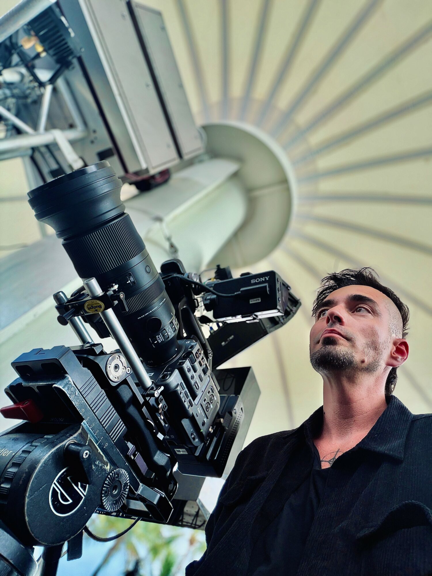 A man operating a large camera in a scientific or medical setting, with a circular structure overhead.