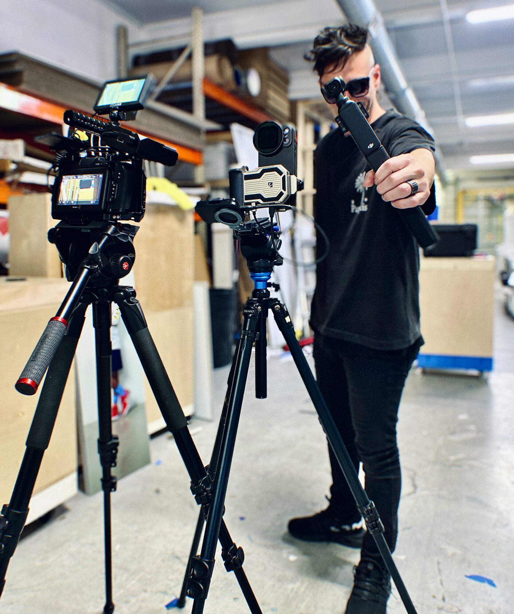 Person adjusting camera equipment in a workshop with shelves and tools in background.