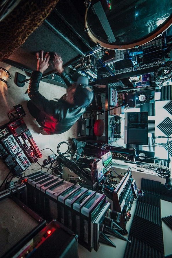 Person working with electronic equipment in a music studio filled with audio gear and instruments.