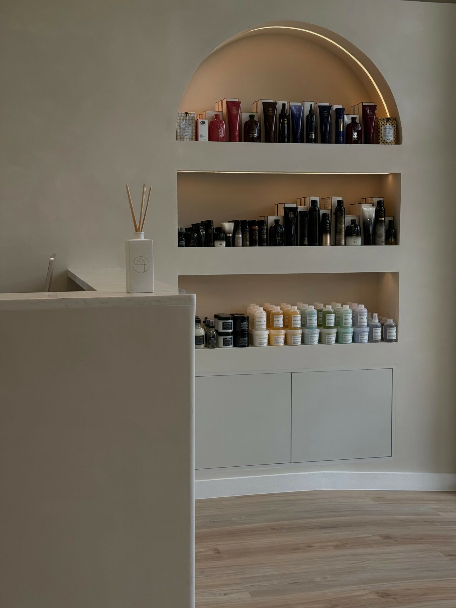 Wall with three shelves holding bottles and containers, and a white cabinet below. Part of a room interior.