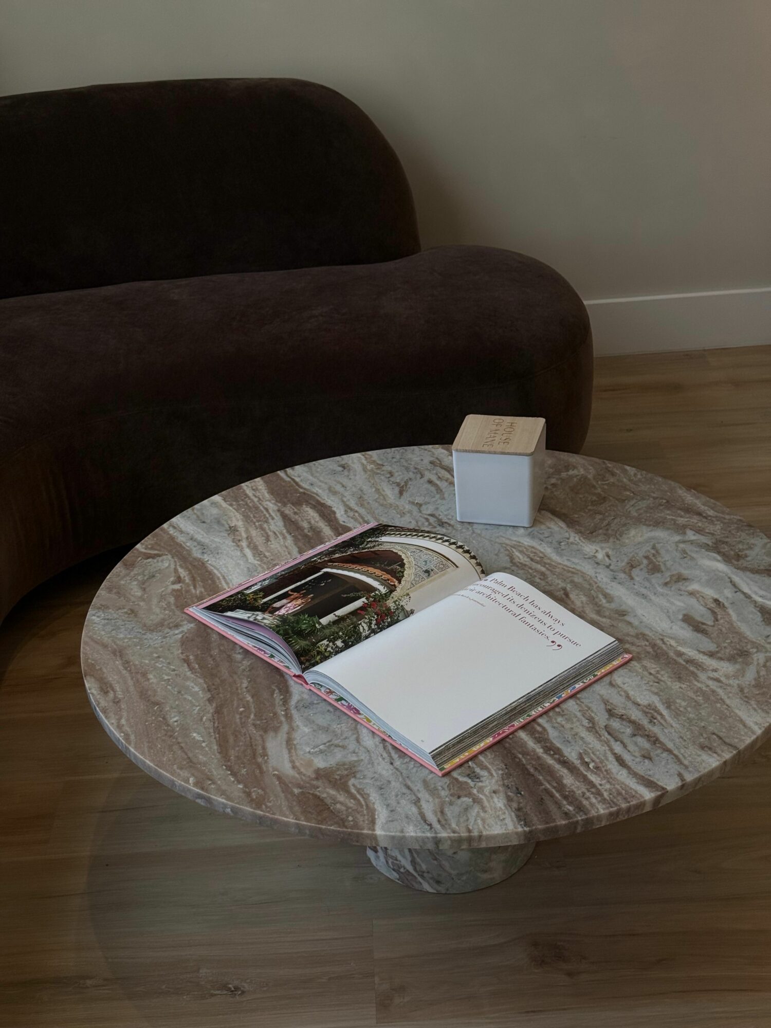Round marble table with open magazine and a small white box, surrounded by two dark chairs, in a room with wooden flooring.