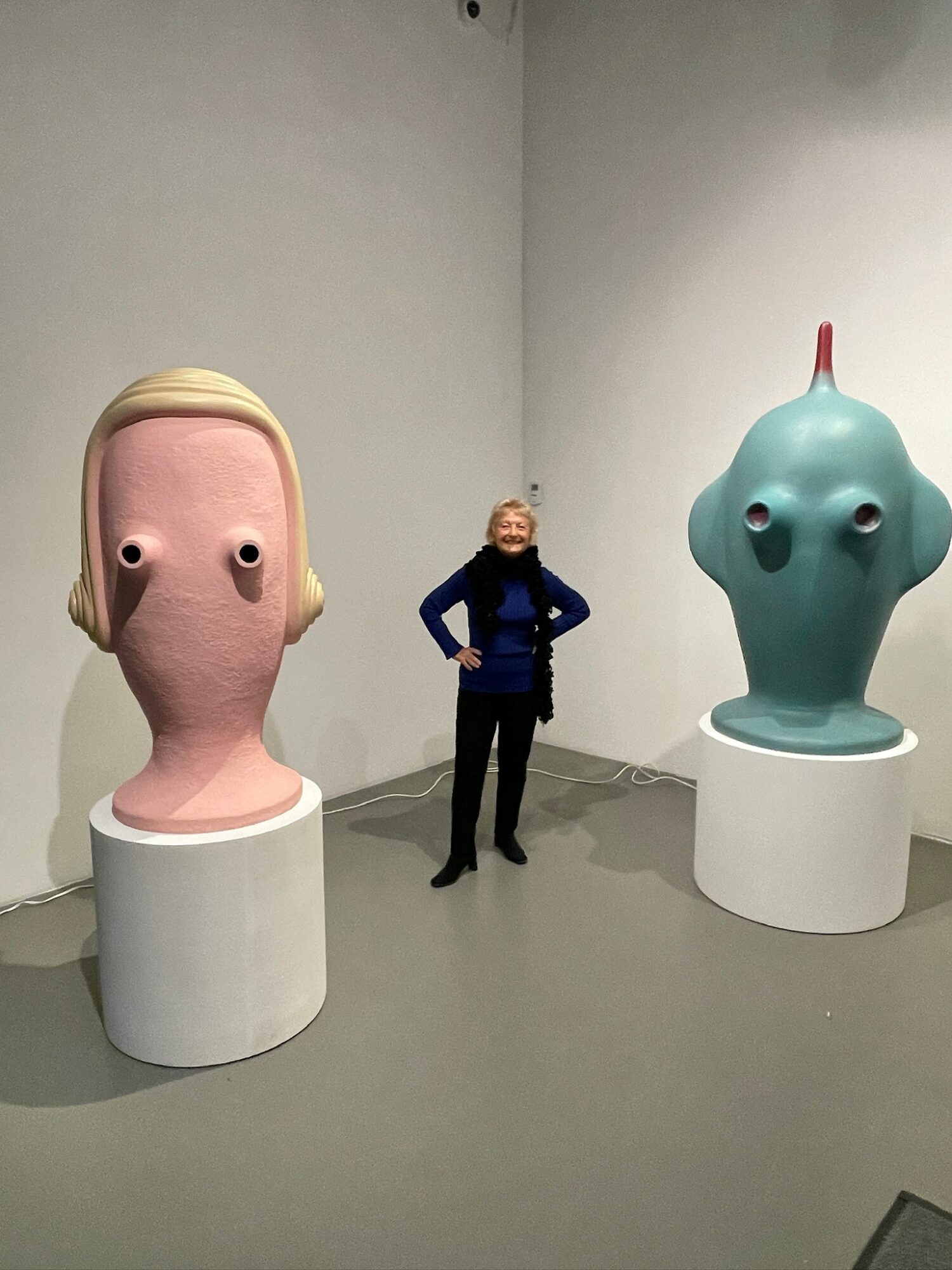 Person standing between two large, colorful sculptures of abstract faces in an art gallery.