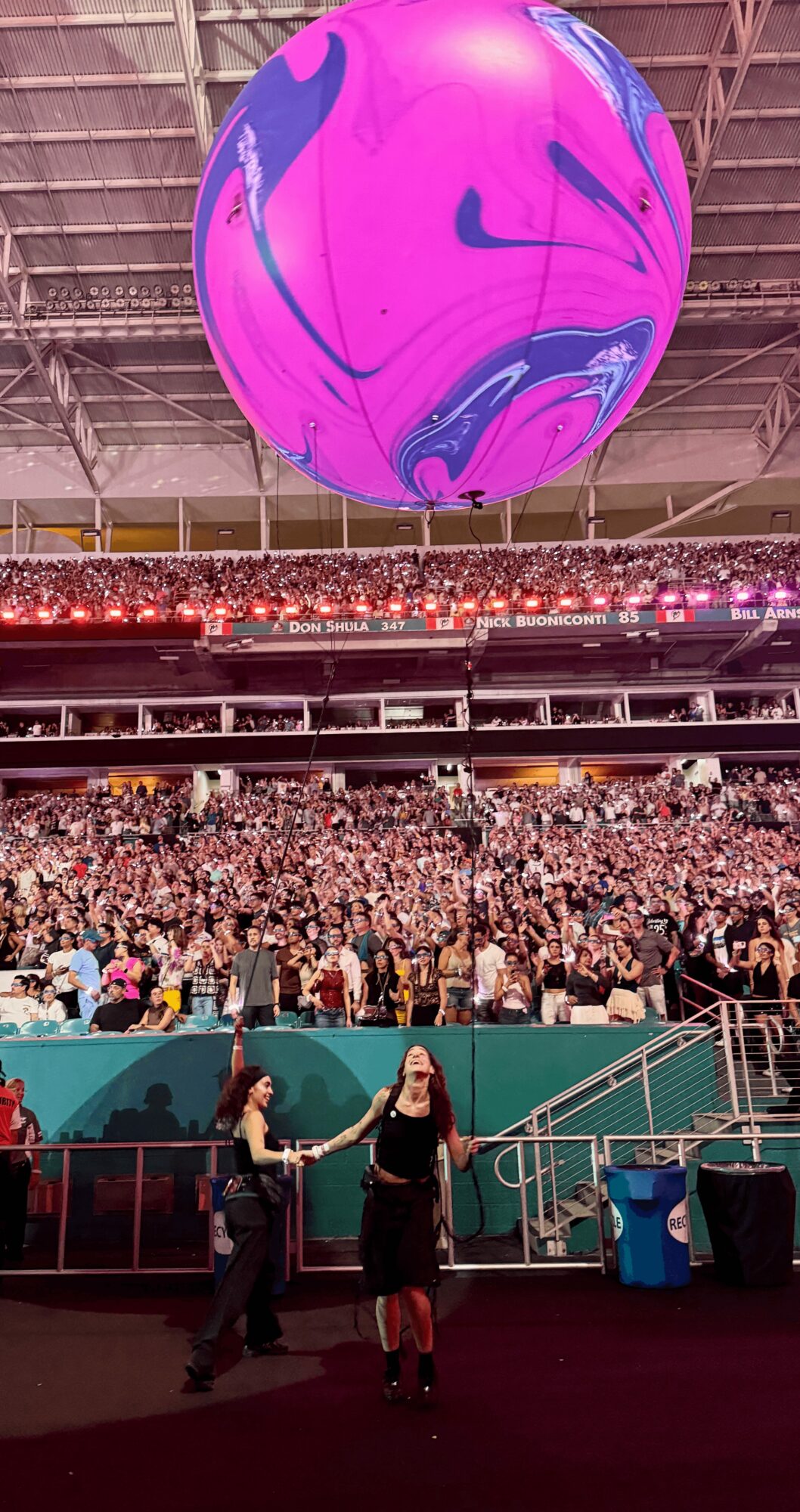 Large purple and blue spherical balloon hanging above a crowded indoor event with people seated and standing.