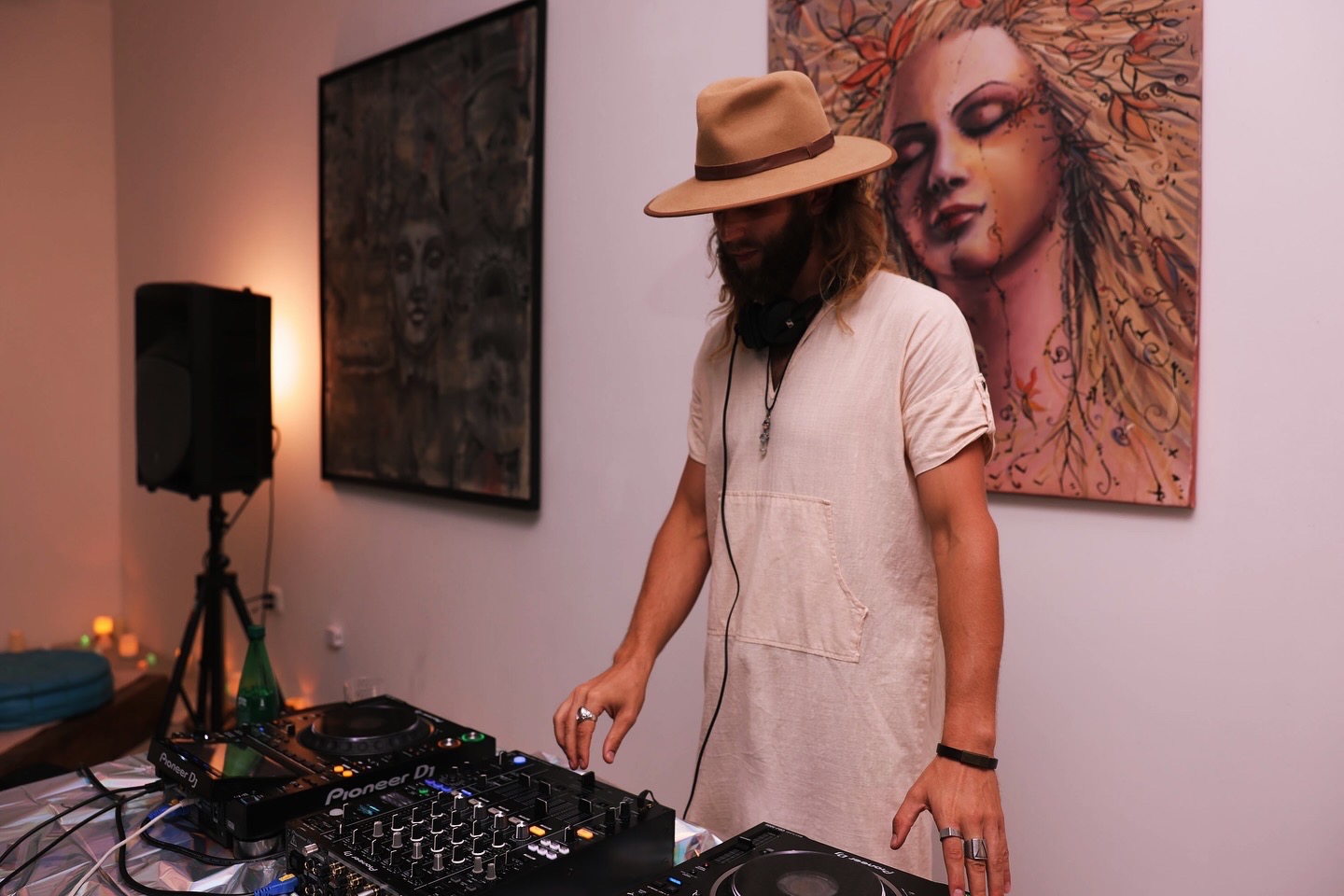Woman wearing a hat and white dress standing next to DJ equipment in an art gallery.