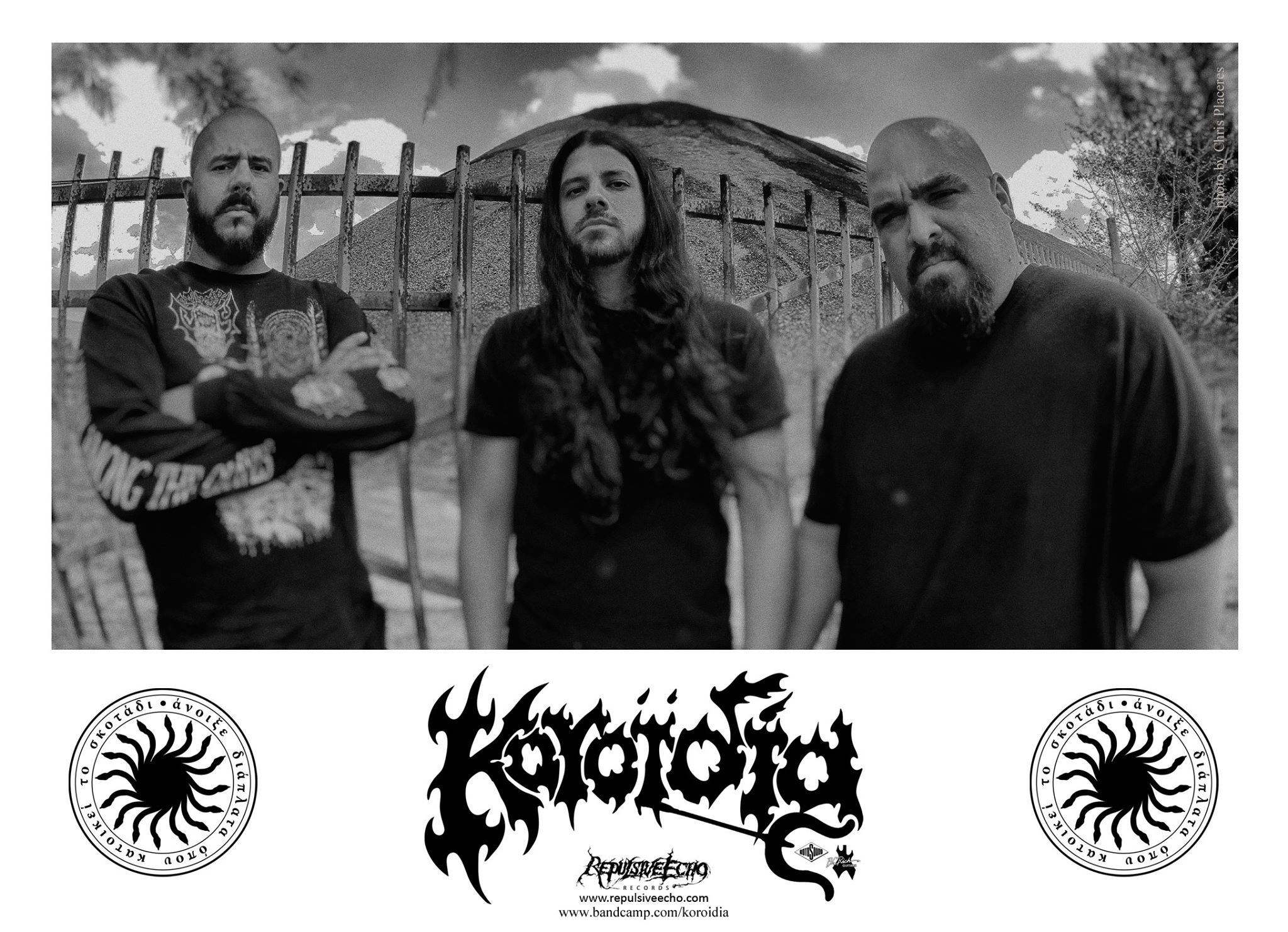 Three people standing outdoors in front of a fence, with a band logo and symbols below, in black and white.