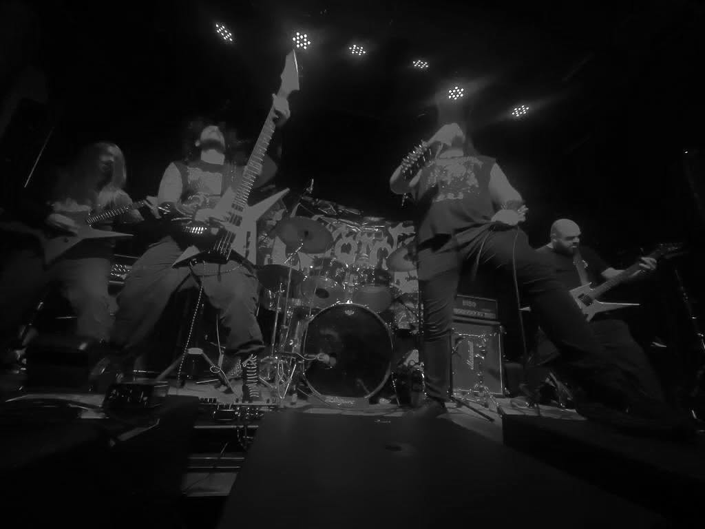 Band performs on stage with instruments, including drums and guitars, in a dark setting with stage lights.