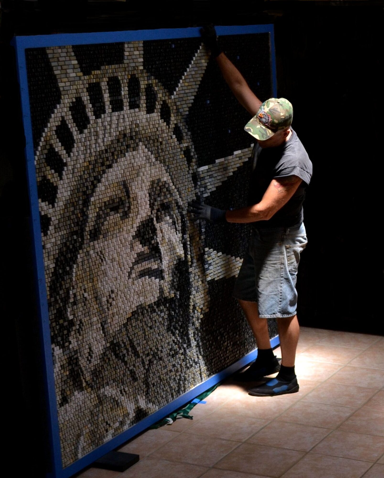 Person creating a mosaic of the Statue of Liberty's face on a large black panel.