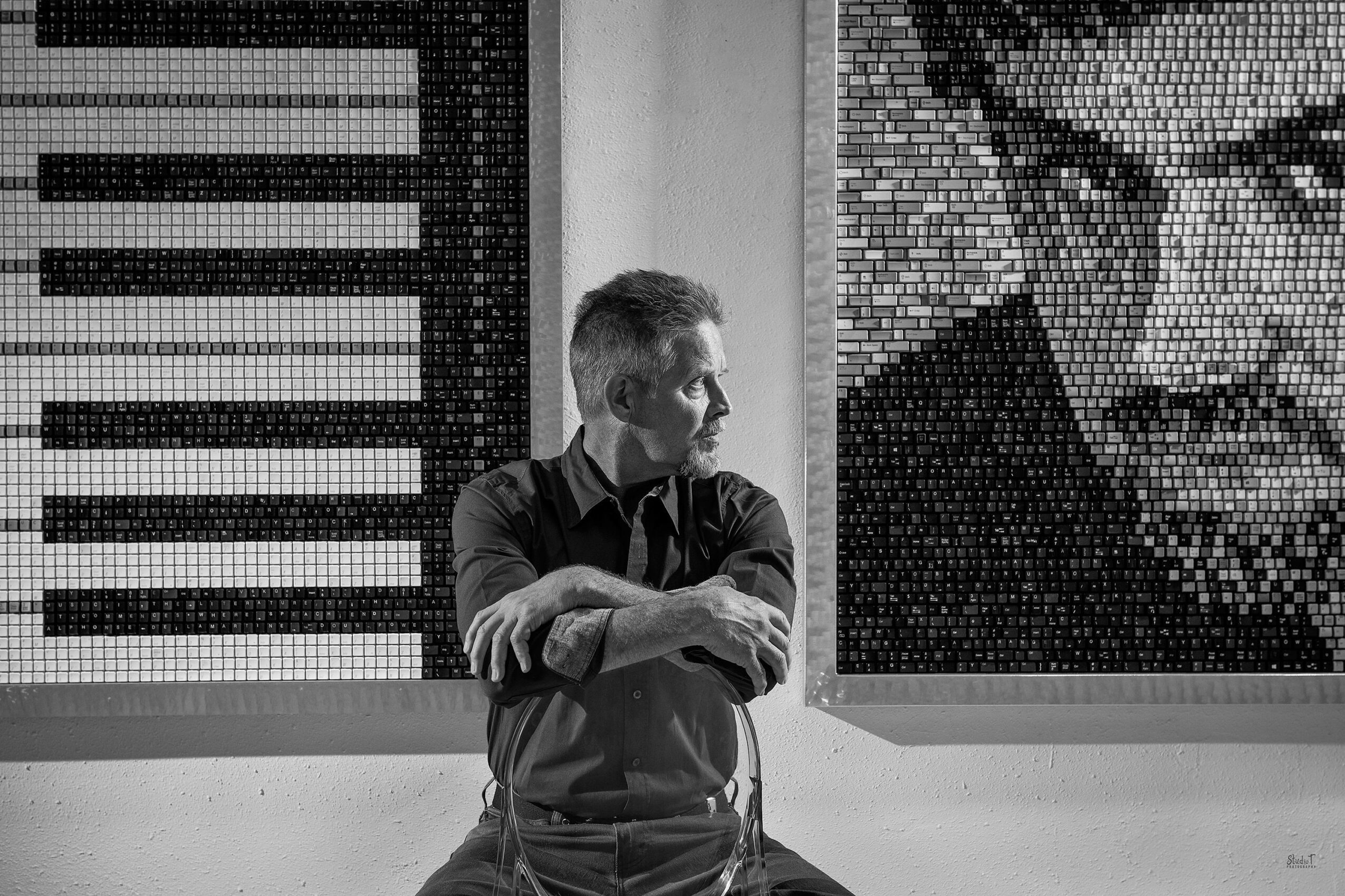 Man with crossed arms looking to the side, artwork with a face in the background, black and white photo.