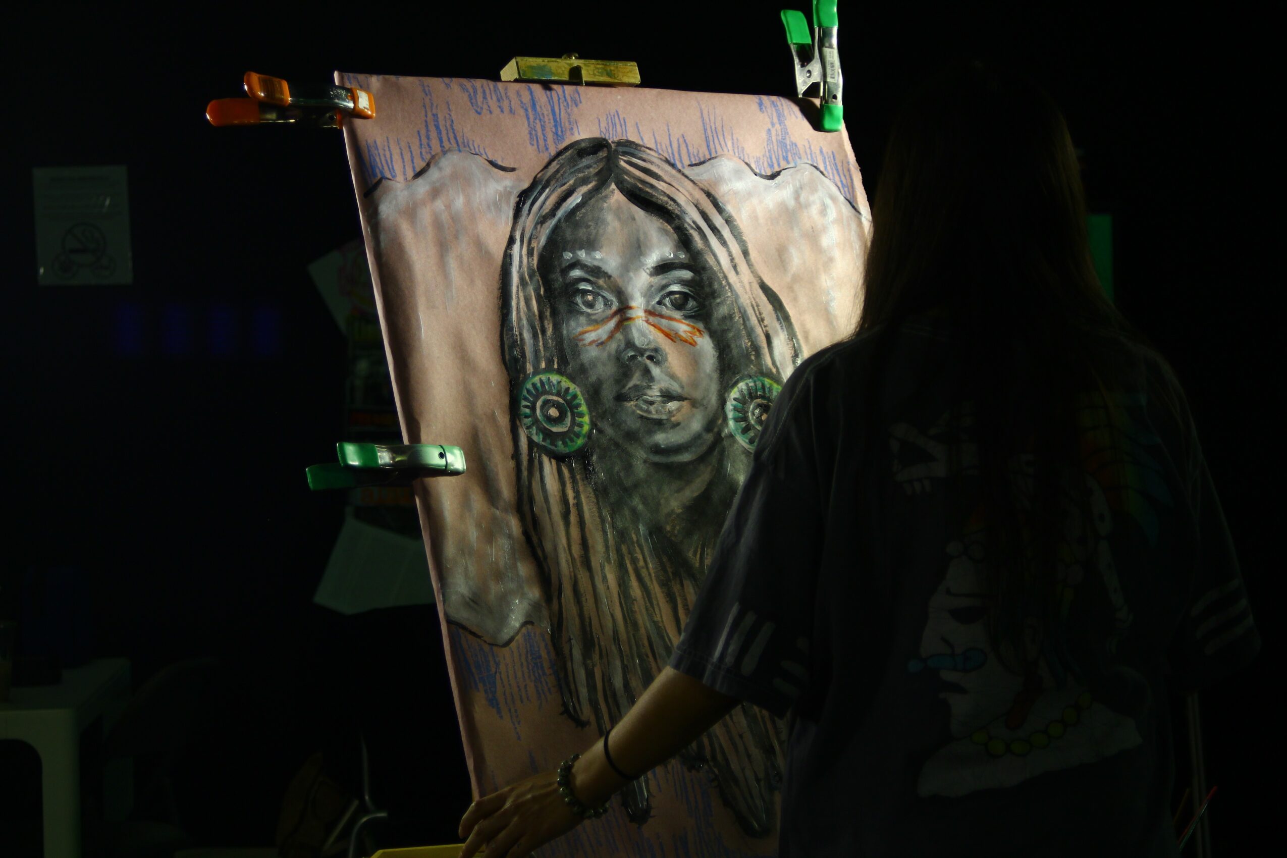 Person working on a portrait painting of a woman with long hair, in a dark environment.