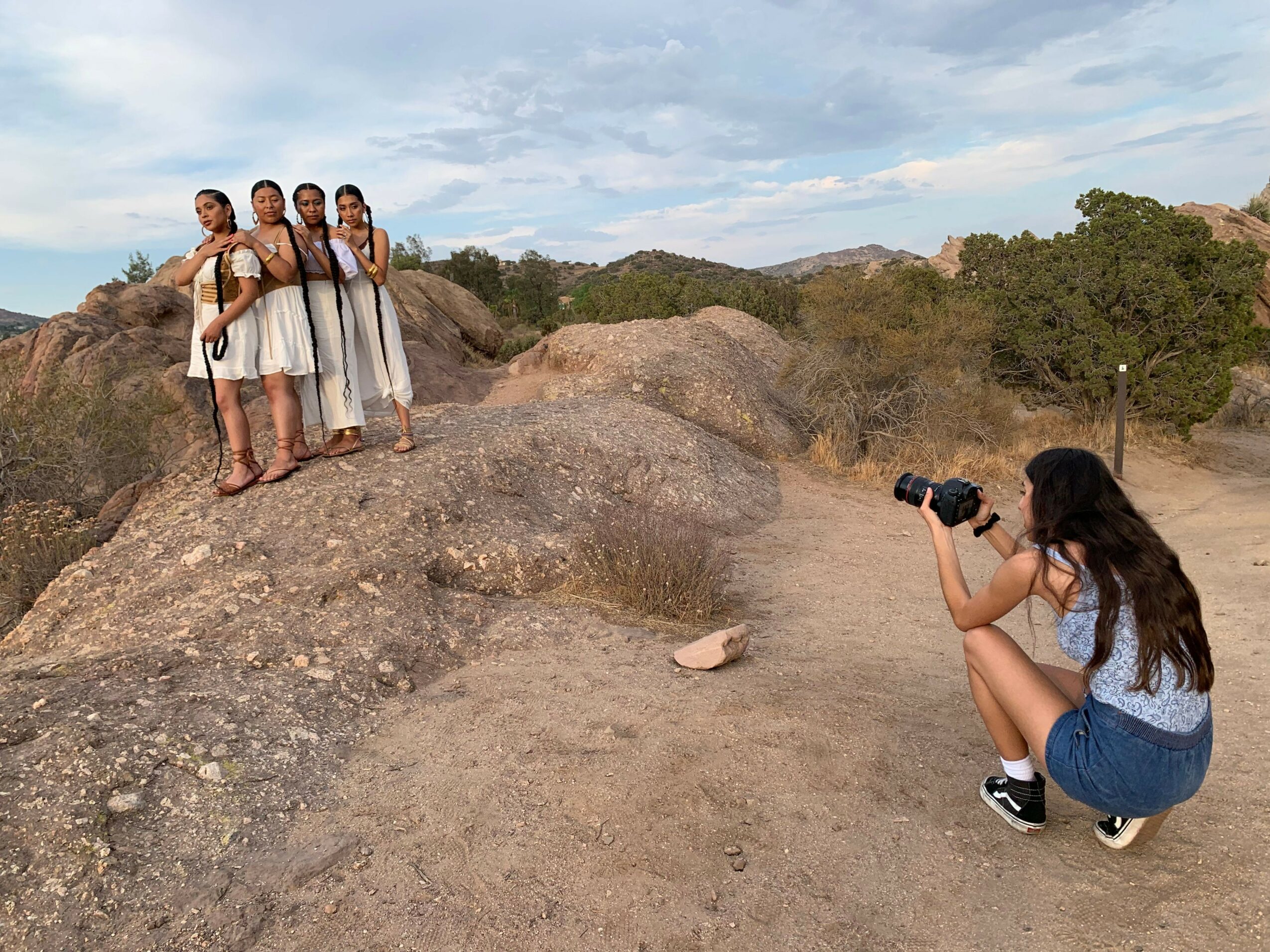 Group of five women standing on rocks, a woman taking a photo, outdoor landscape with hills and trees