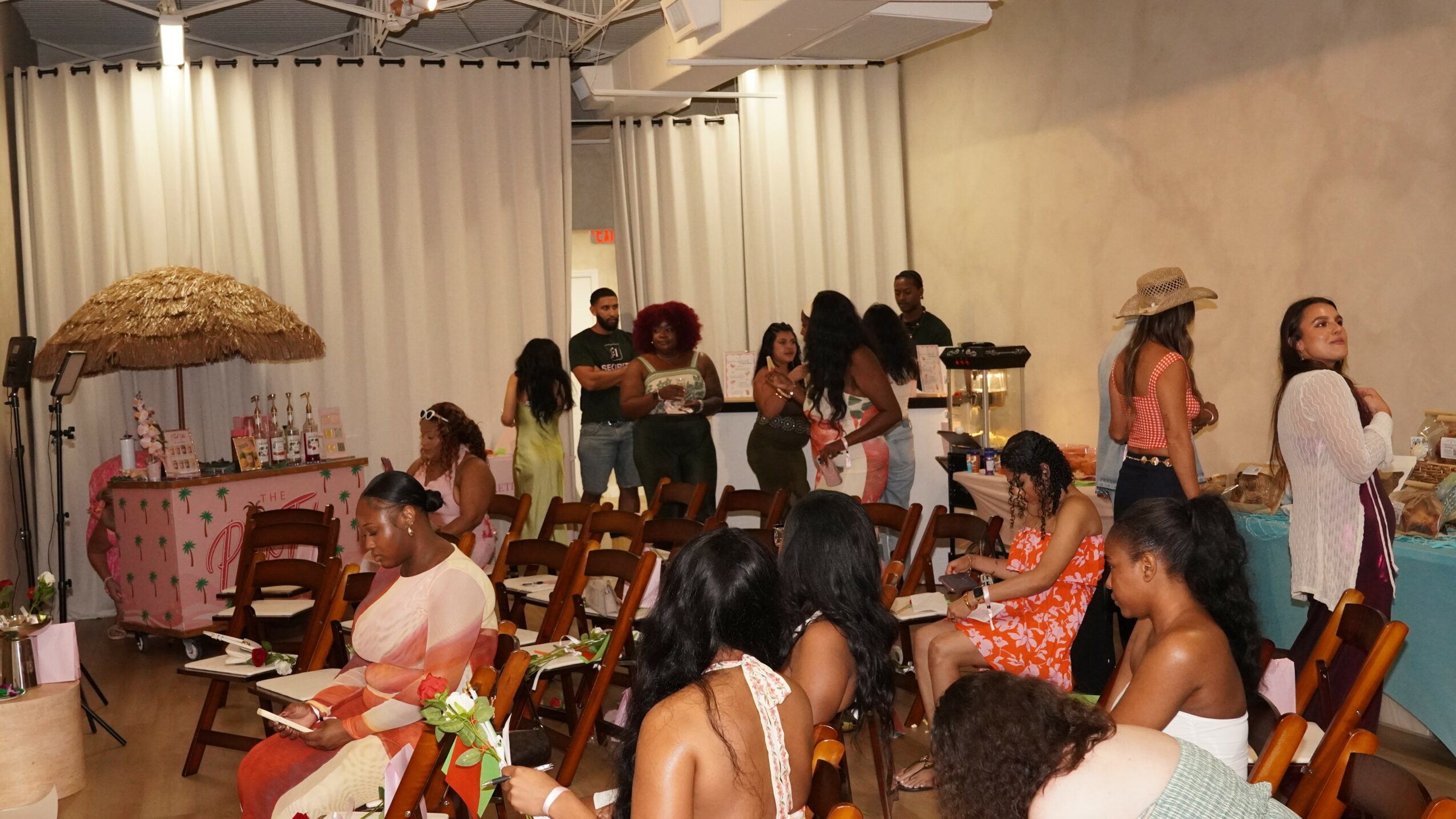 Group of women and children gathered in a room with chairs and tables, some standing and some sitting, engaged in activities.