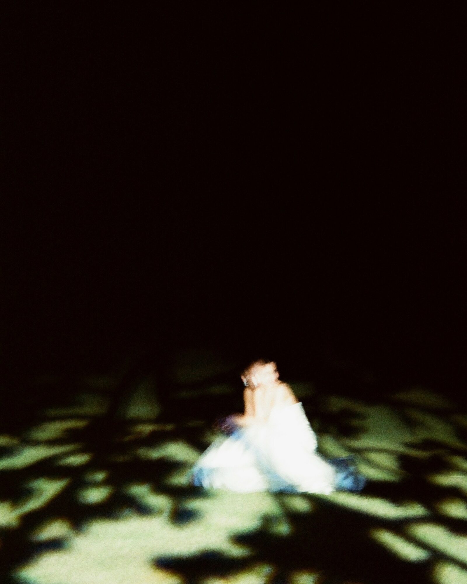 Person sitting on the floor in a dark room with patterned light projections, wearing a light-colored outfit.