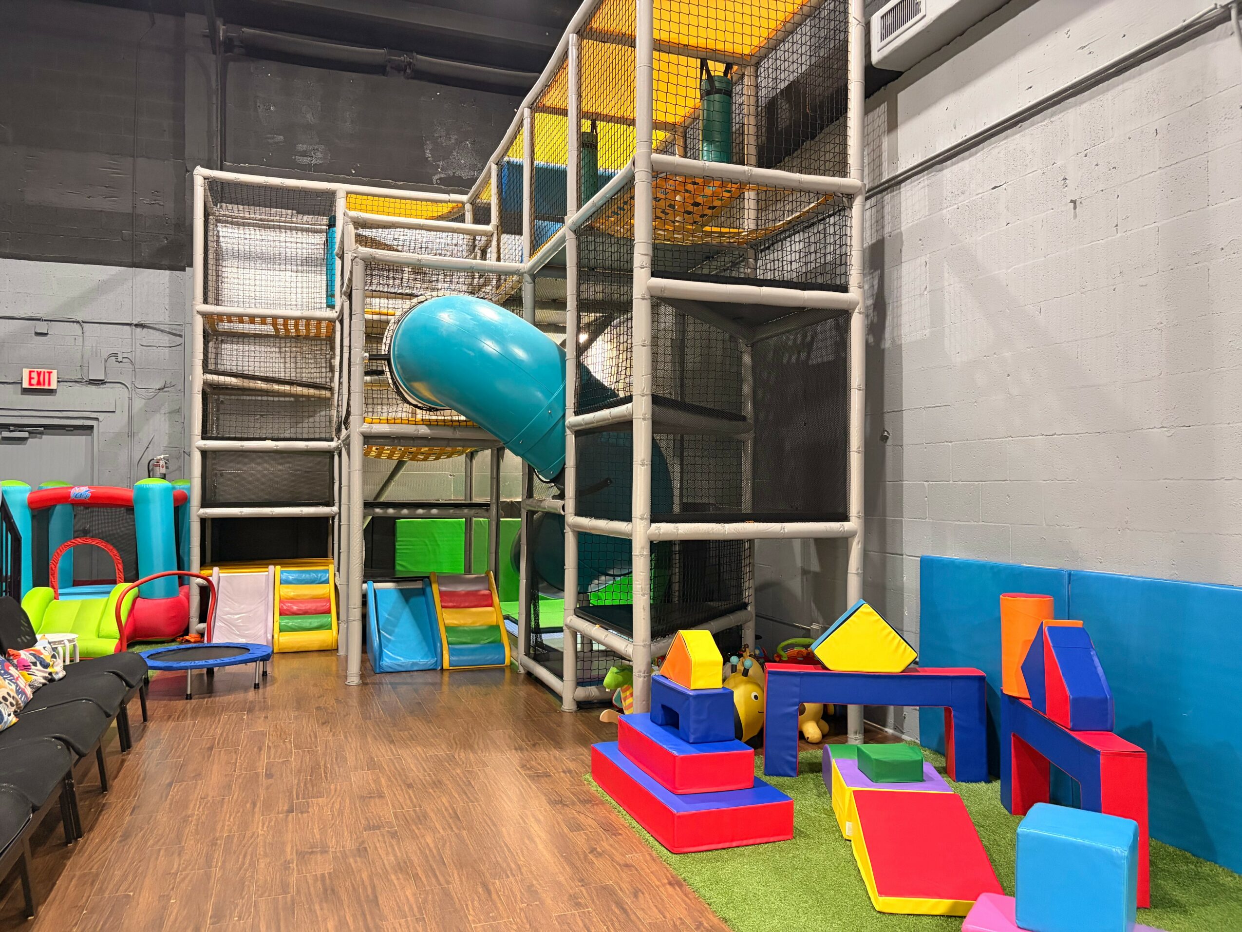 Indoor play area with climbing structure, foam blocks, and colorful toys on a wooden floor.