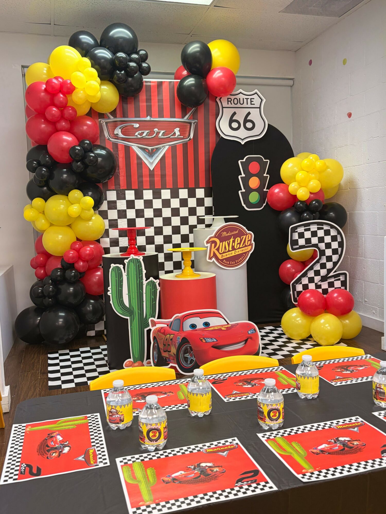 Party table with Lightning McQueen decorations, checkered patterns, and themed balloons in red, yellow, and black colors.