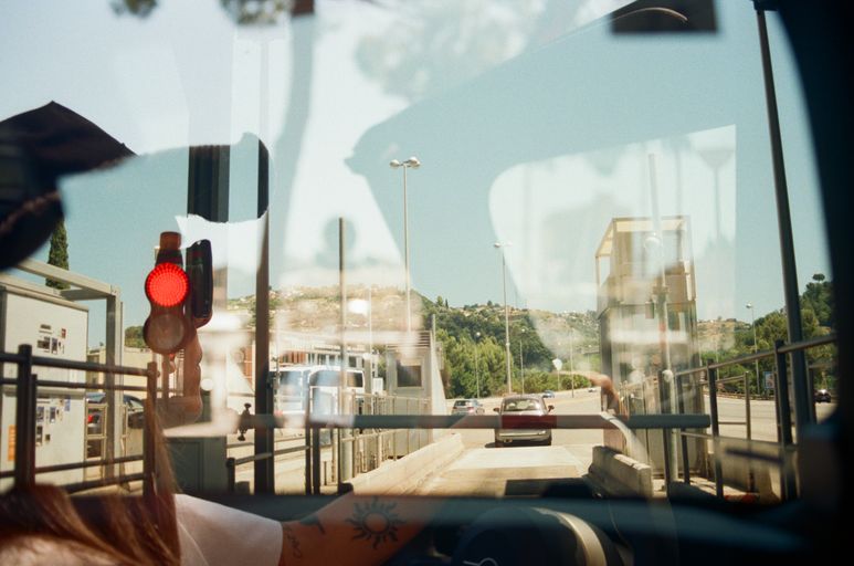 View through a vehicle windshield showing a road with cars, traffic light, and buildings in the distance.